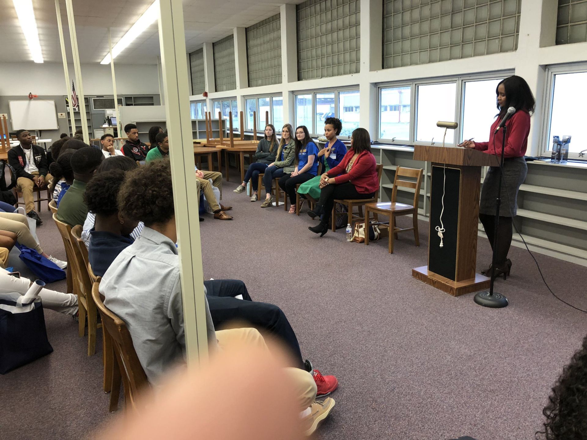 A woman is standing at a podium giving a speech to a group of people sitting in chairs.