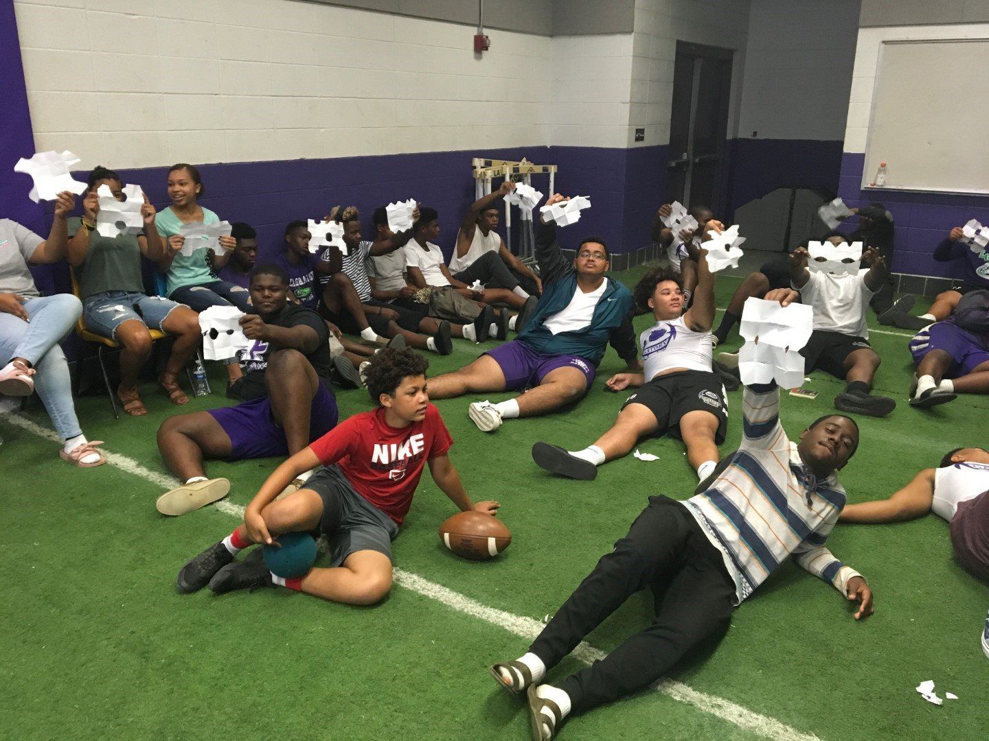 A group of people are sitting on a football field holding pieces of paper.
