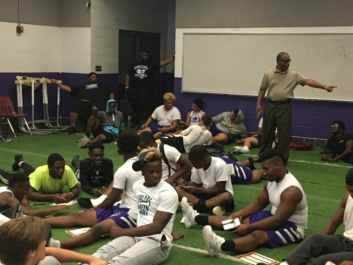A group of people are sitting on the floor in a gym.