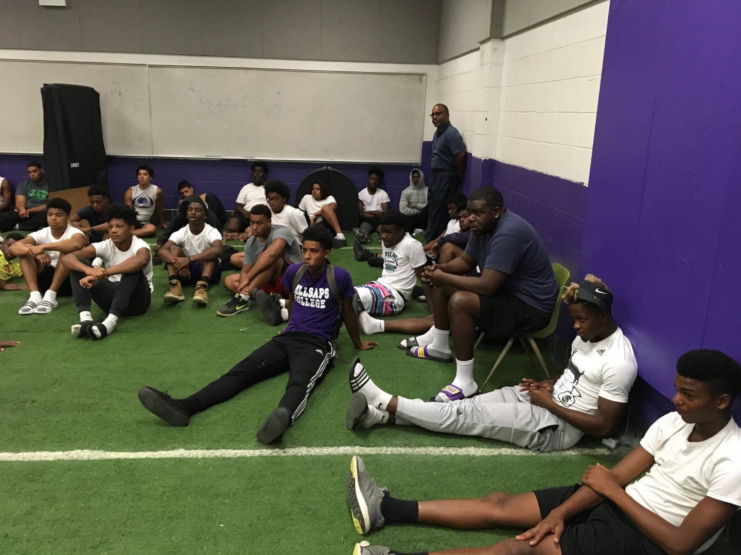A group of young men are sitting on the grass in a gym.