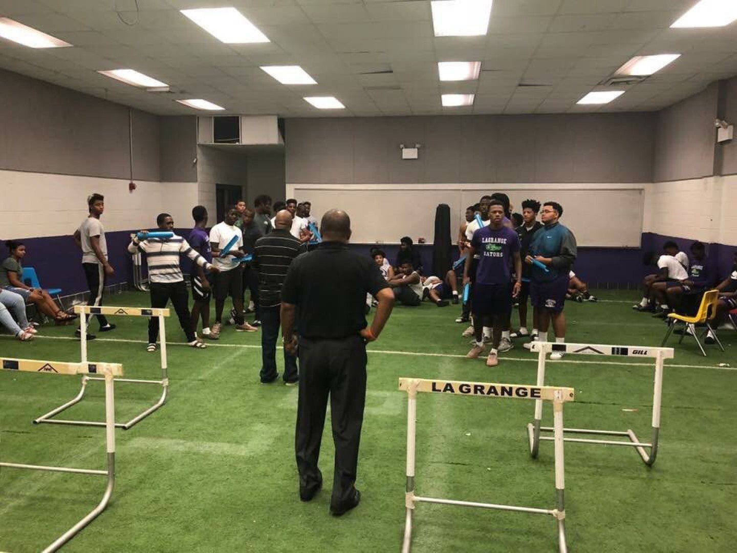 A man is standing in a gym talking to a group of people.