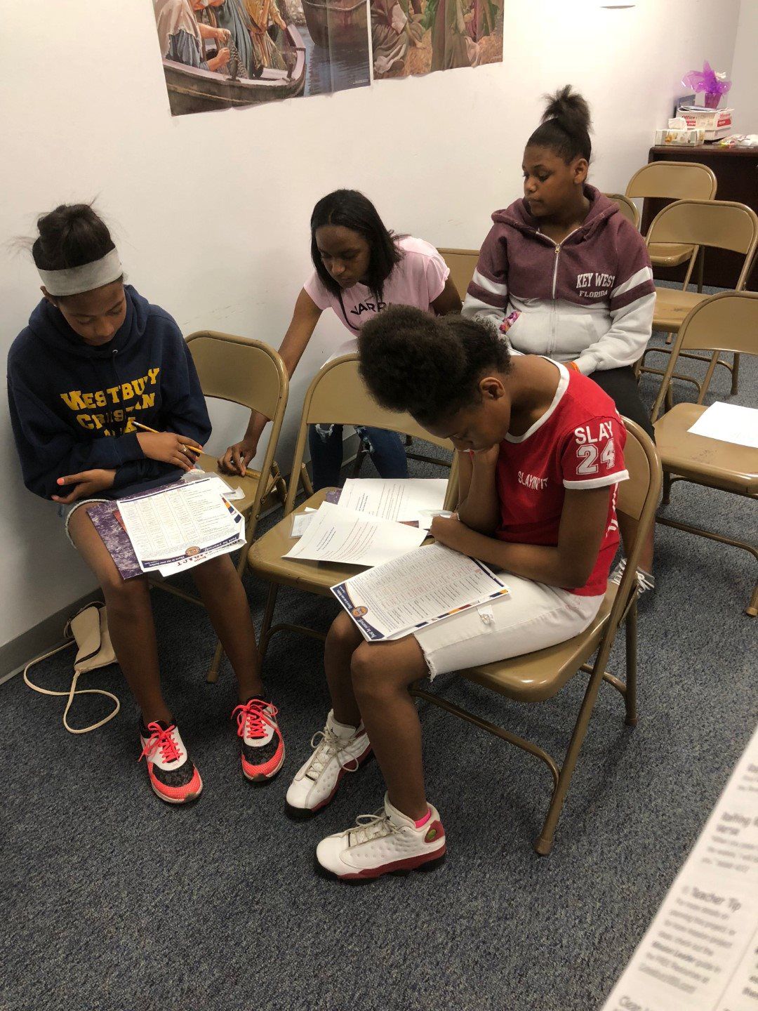 A group of young girls are sitting in chairs reading books.
