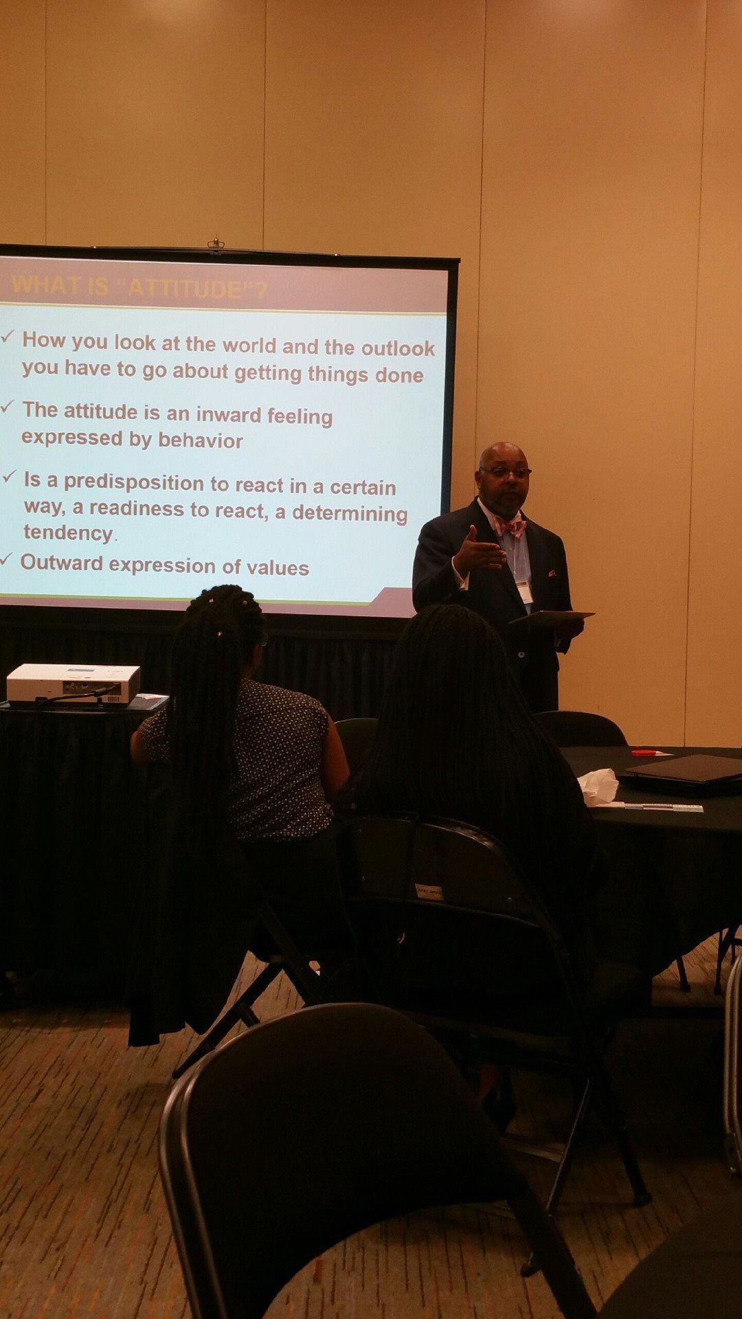 A man is giving a presentation to a group of people in front of a projector screen.