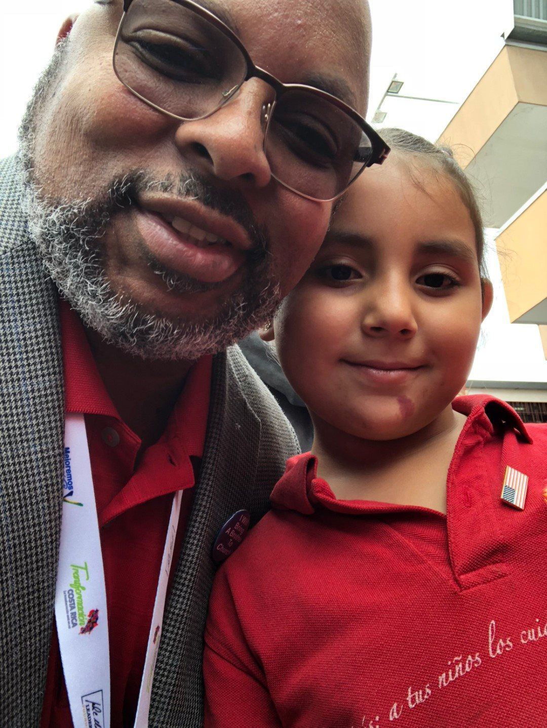 A man and a little girl are posing for a picture and the little girl is wearing a red shirt that says niños los amo