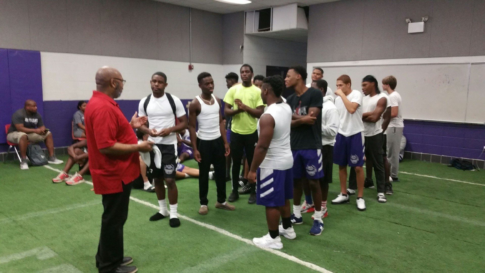A man in a red shirt is talking to a group of men on a football field.