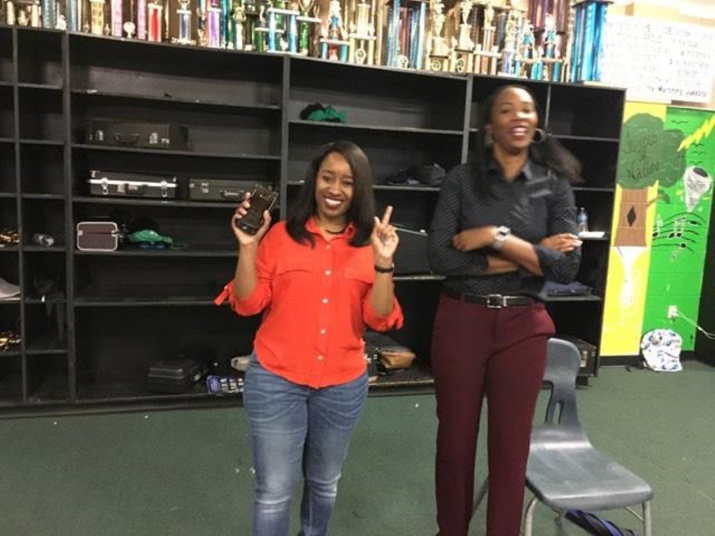 Two women are standing next to each other in front of a trophy wall.