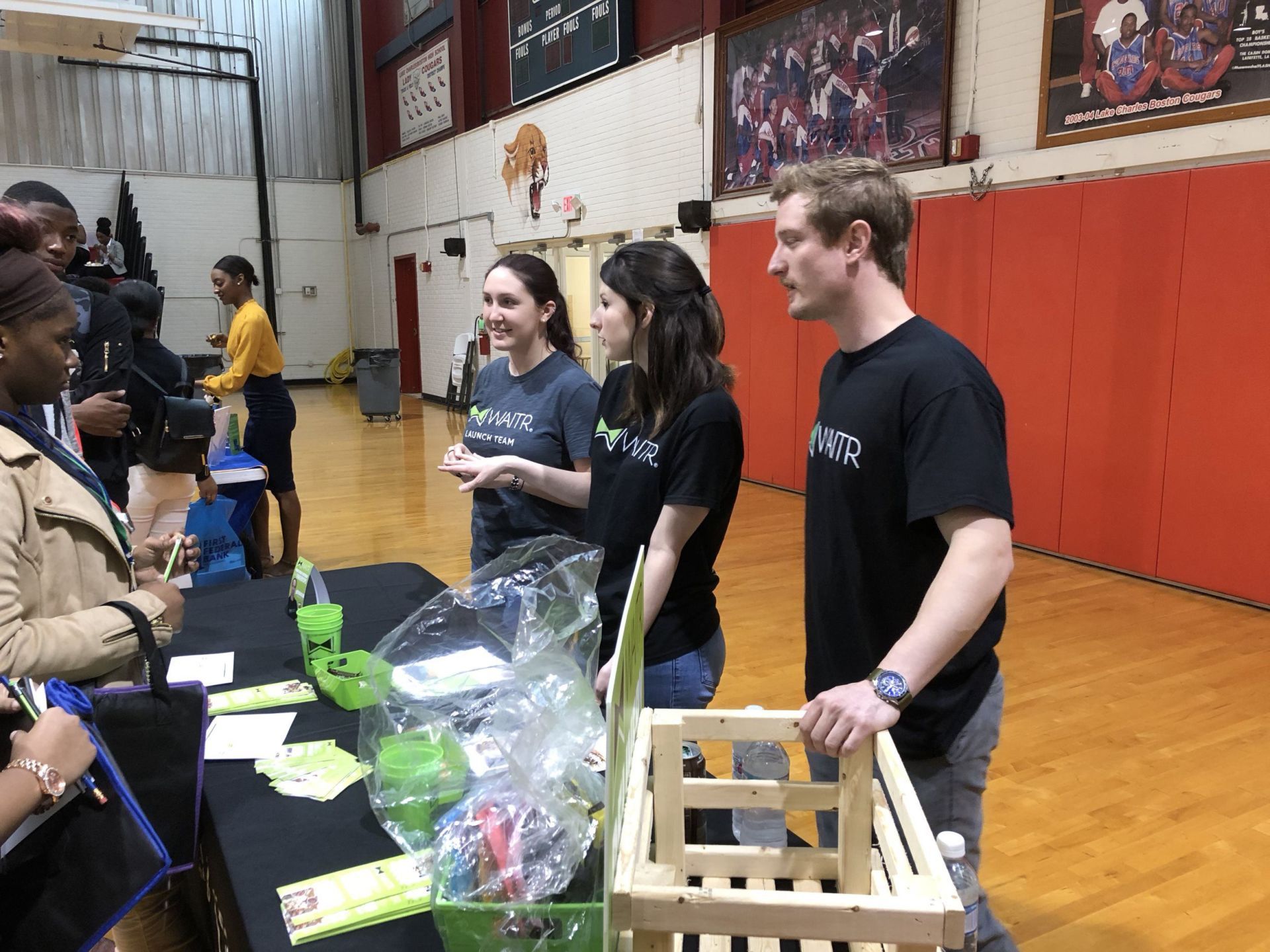 A group of people are standing around a table in a gym.