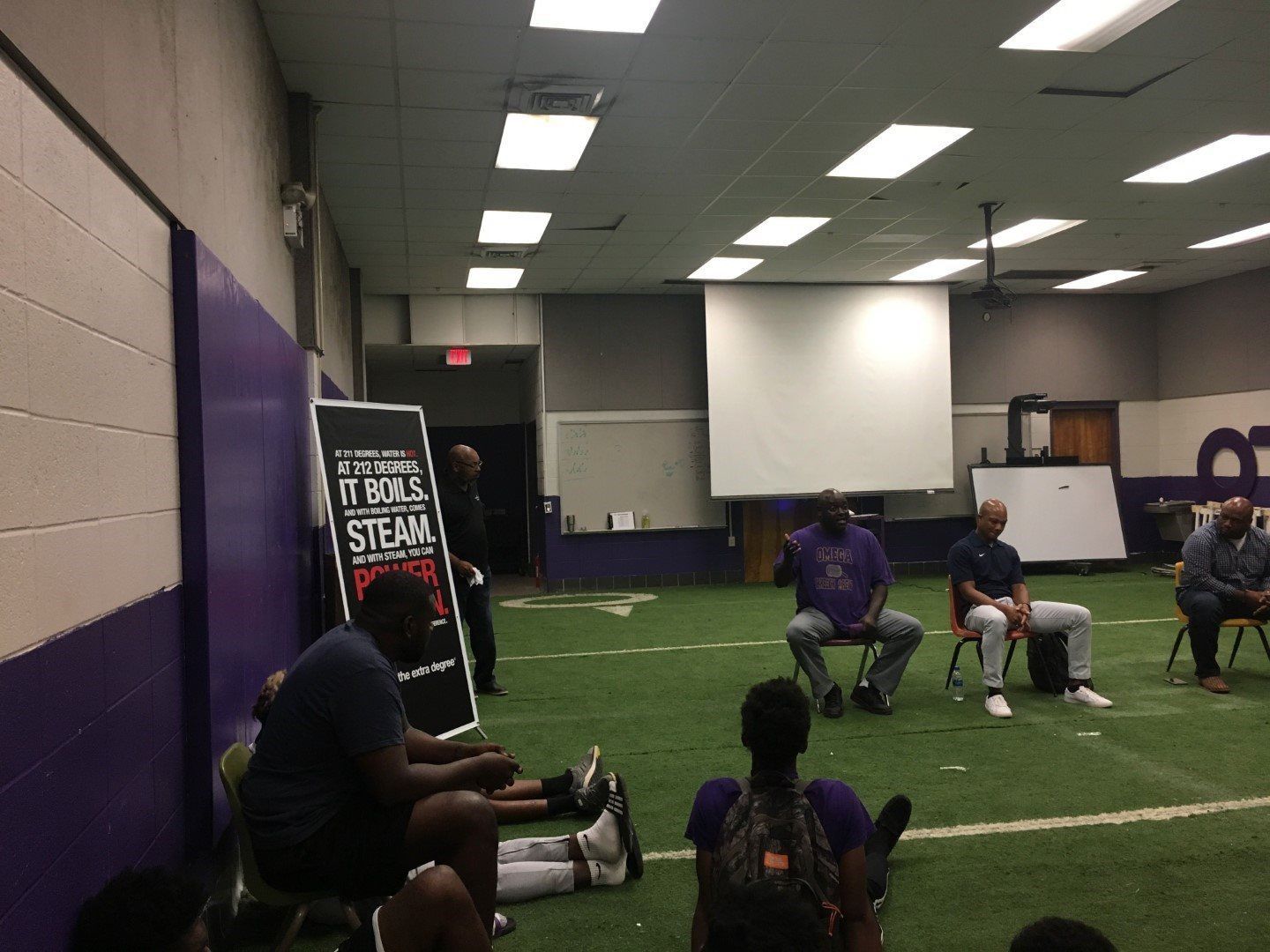 A group of people are sitting in a room with a projector screen.