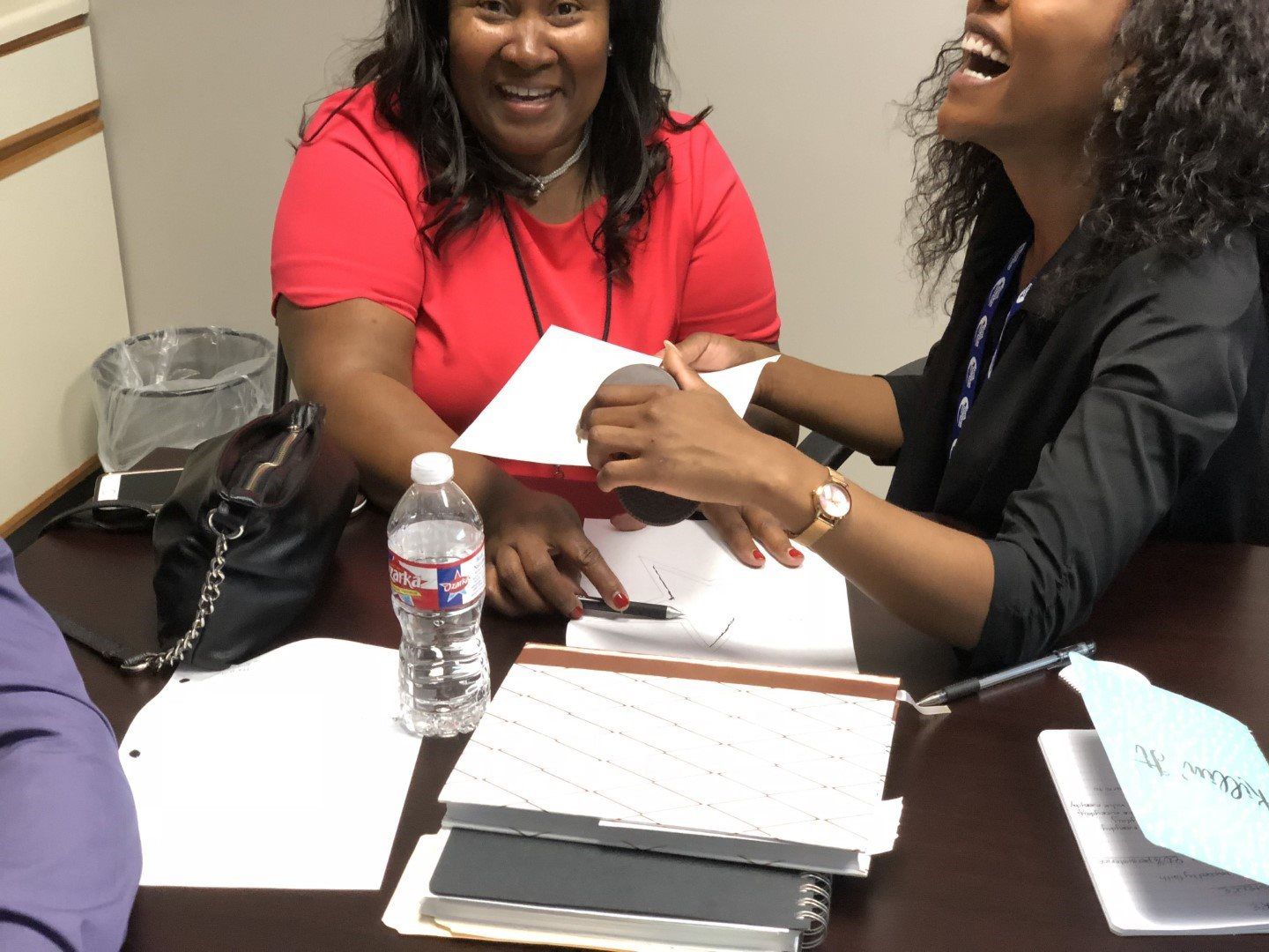Two women are sitting at a table with papers and a water bottle
