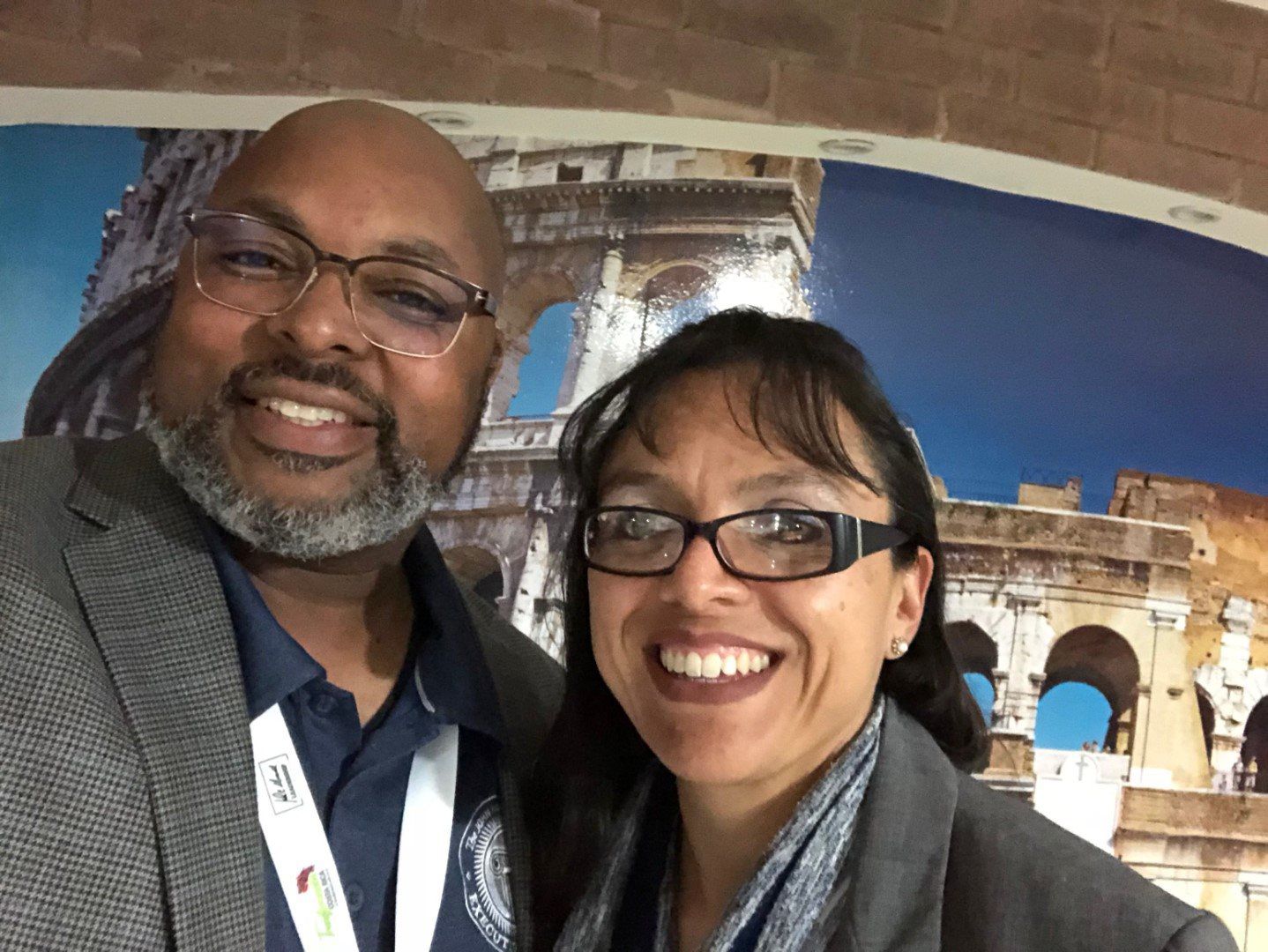 A man and a woman are posing for a picture in front of a picture of the colosseum