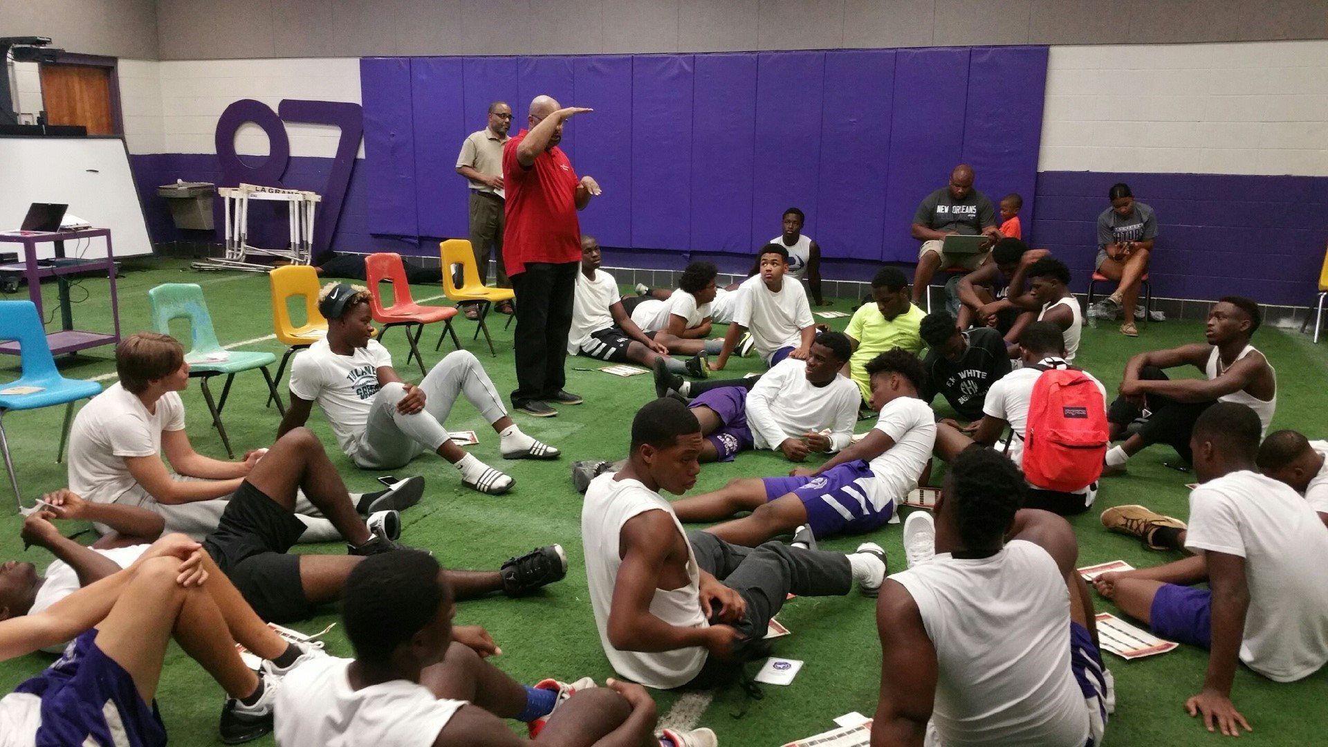 A group of young men are sitting in a circle on the floor in a gym.