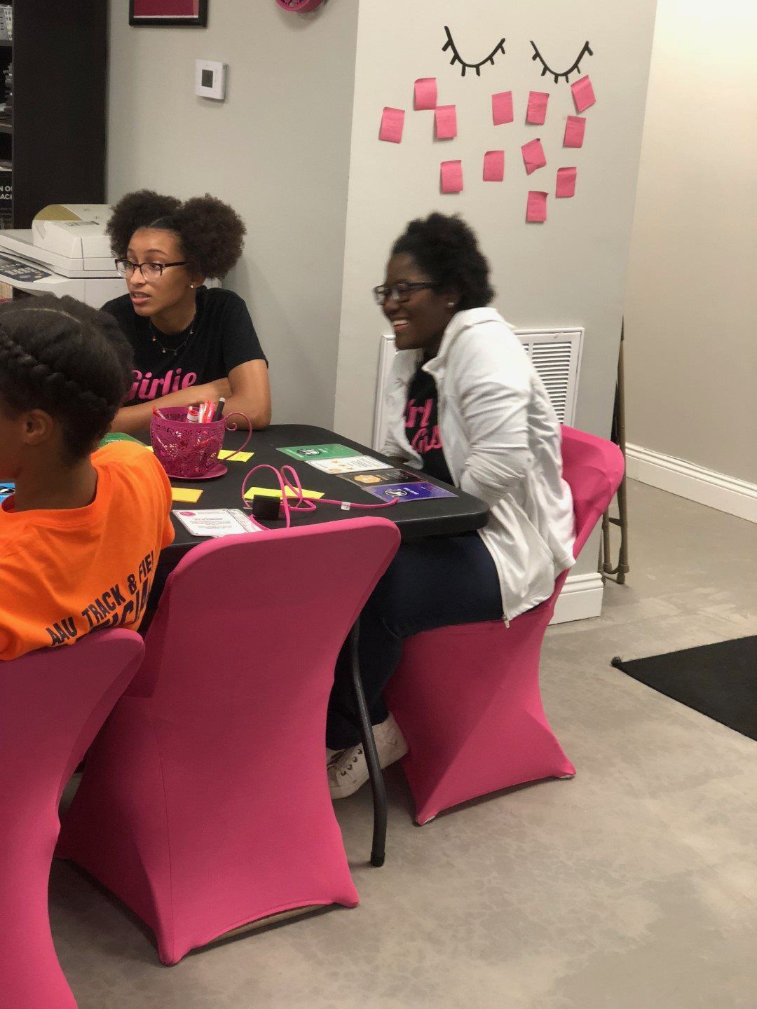 A group of people are sitting at a table with pink chairs.