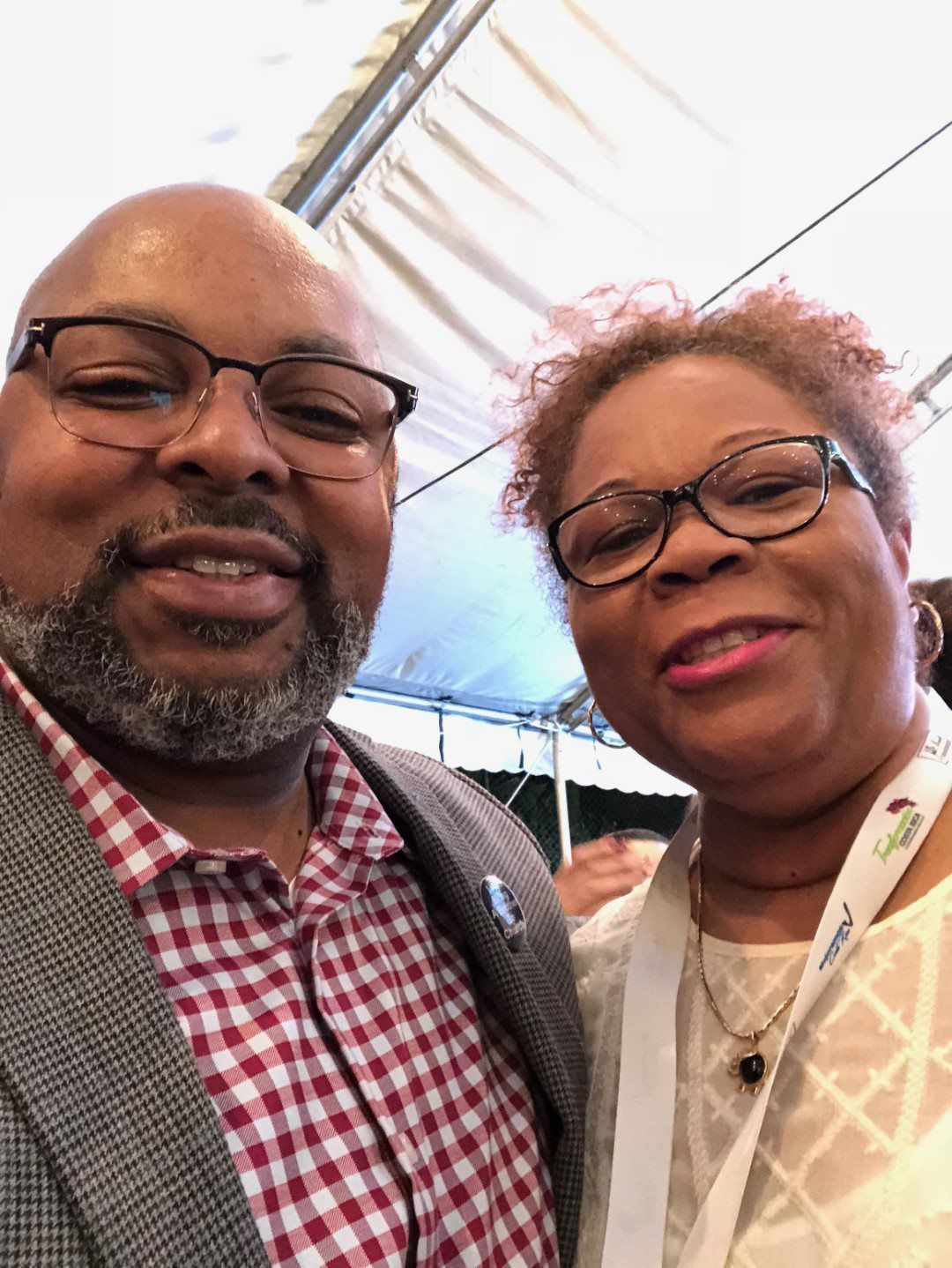 A man and a woman are posing for a selfie under a tent.