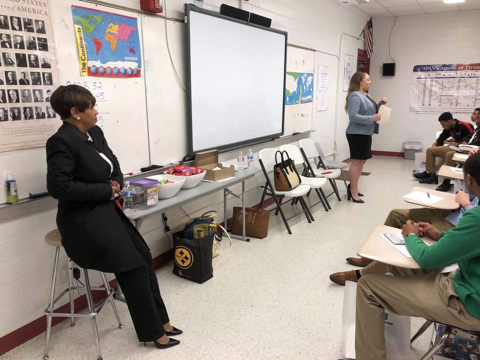 A woman is giving a presentation to a group of students in a classroom.