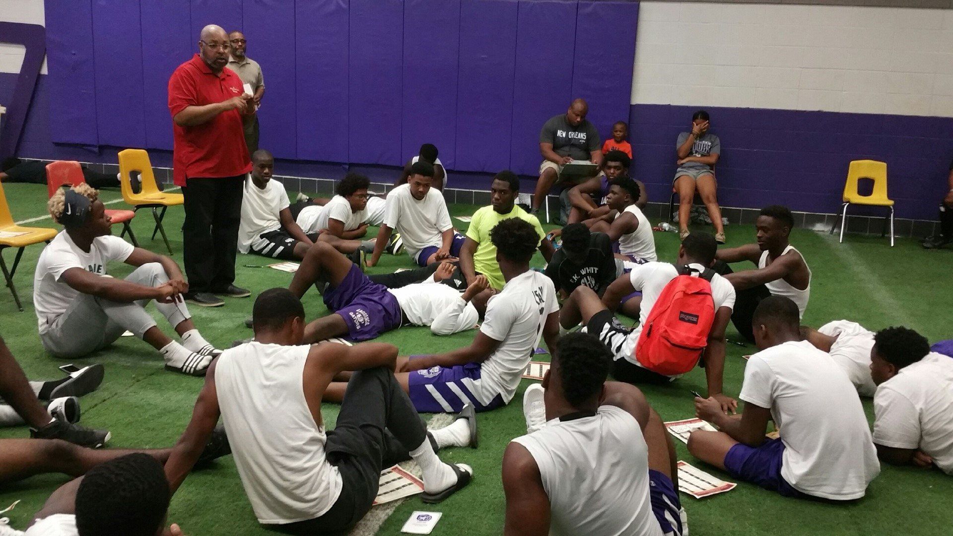 A man in a red shirt is talking to a group of young men