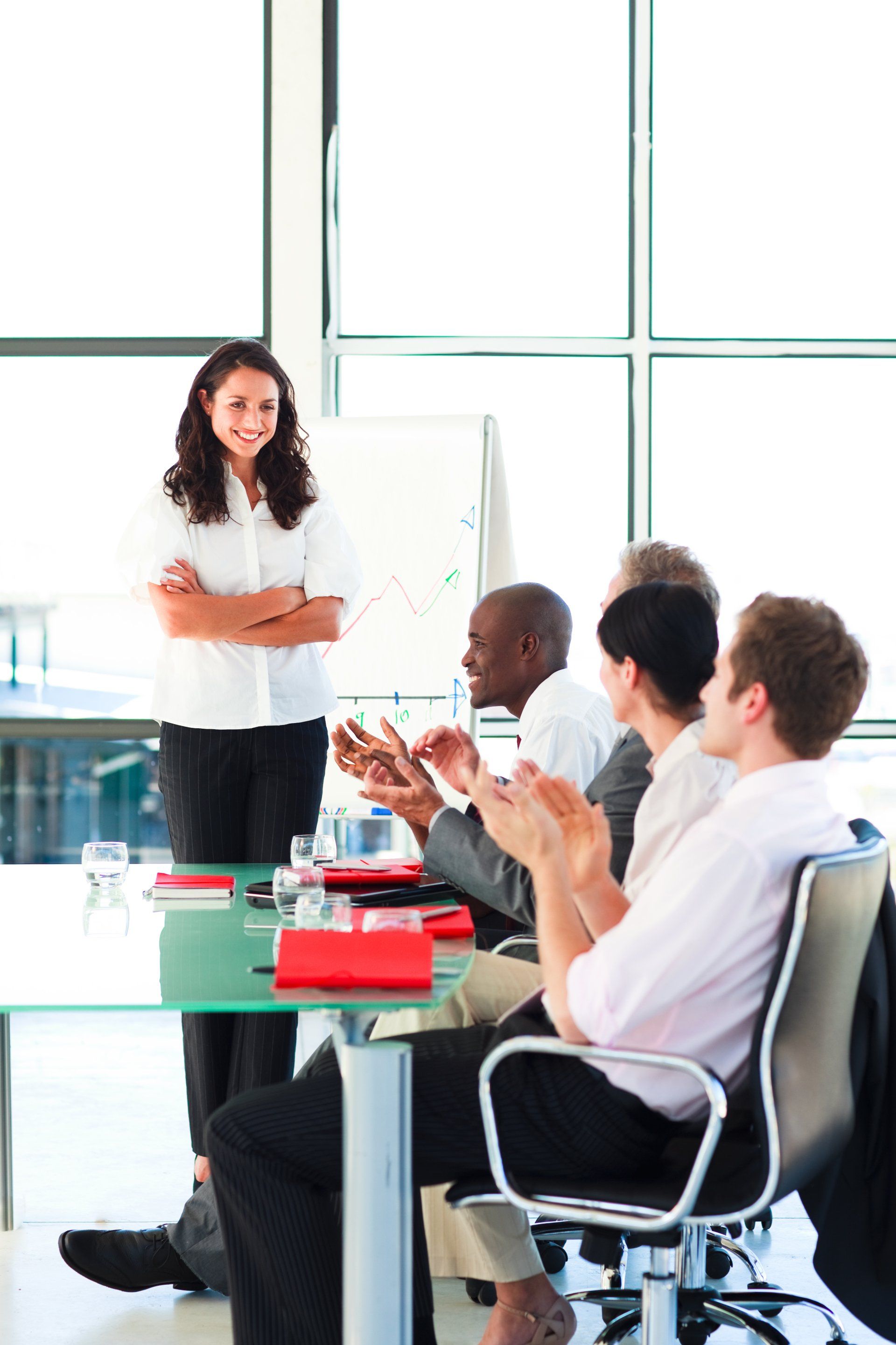 A woman is giving a presentation to a group of people sitting around a table.