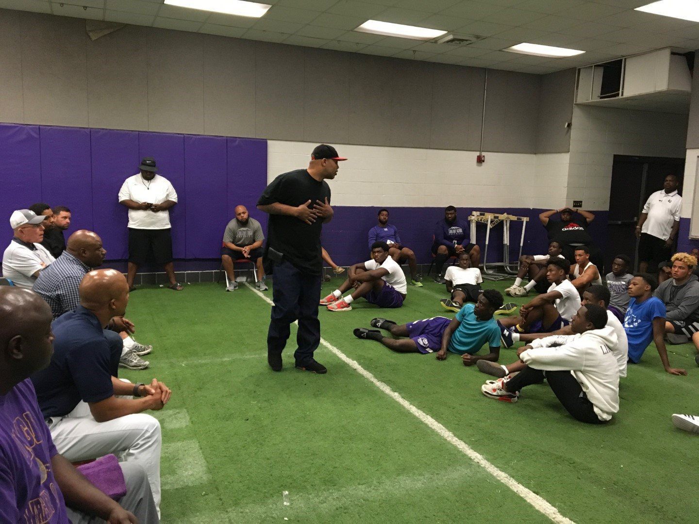 A man is standing in front of a group of people sitting on the floor.