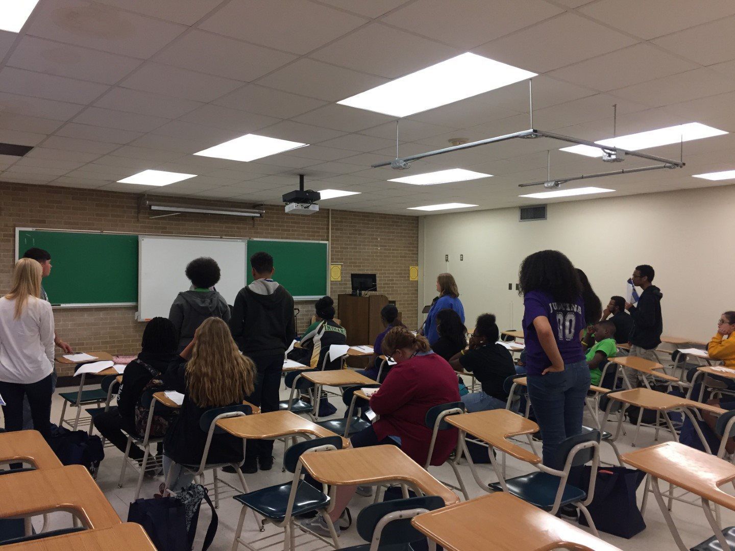 A group of students are standing in a classroom with one wearing a number 10 jersey