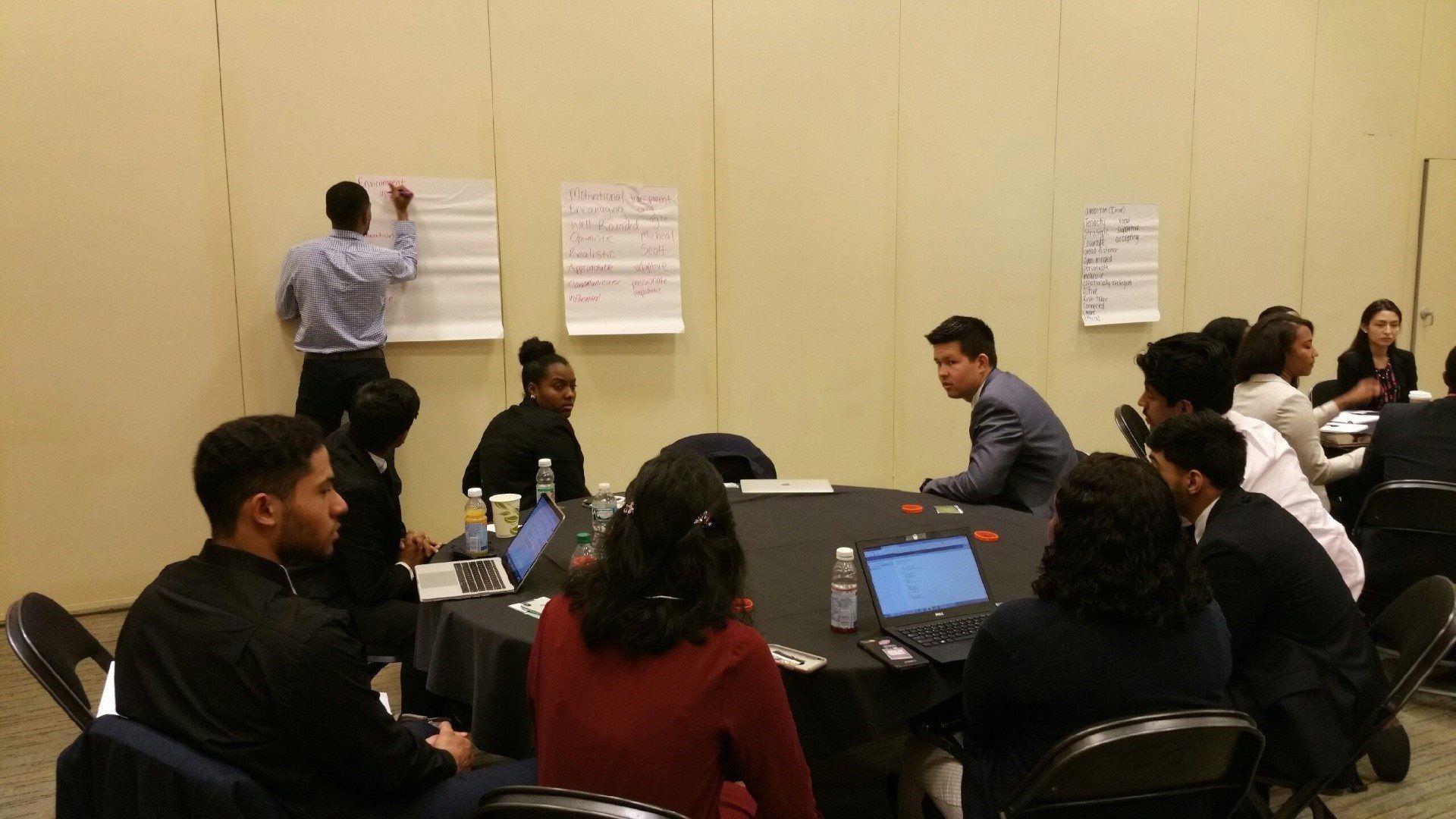 A group of people are sitting around a table with laptops.