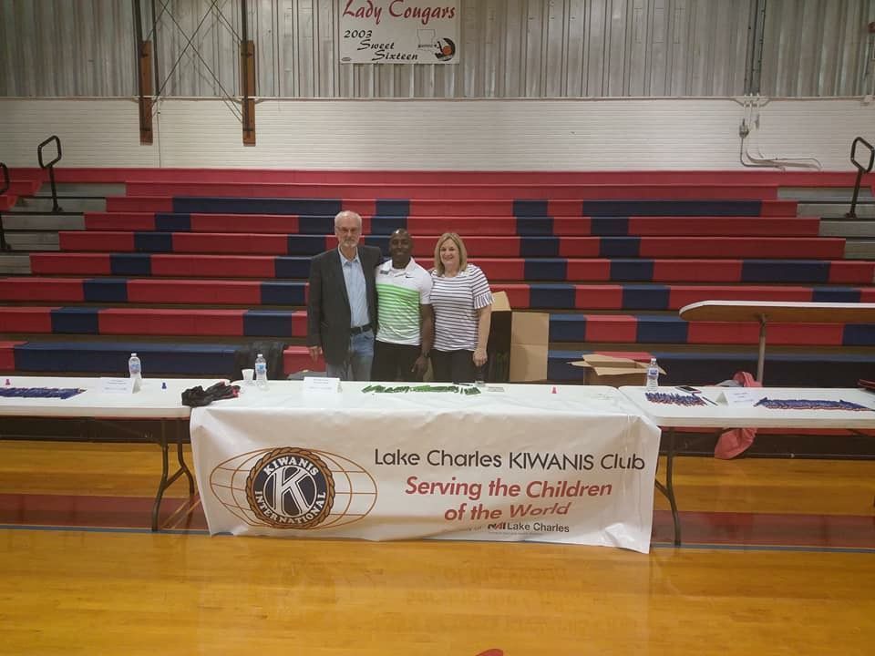 A group of people standing in front of a table that says lake charles kiwanis club serving the children of the world