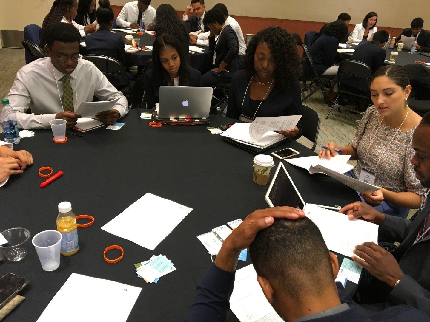 A group of people are sitting around a table with laptops and papers