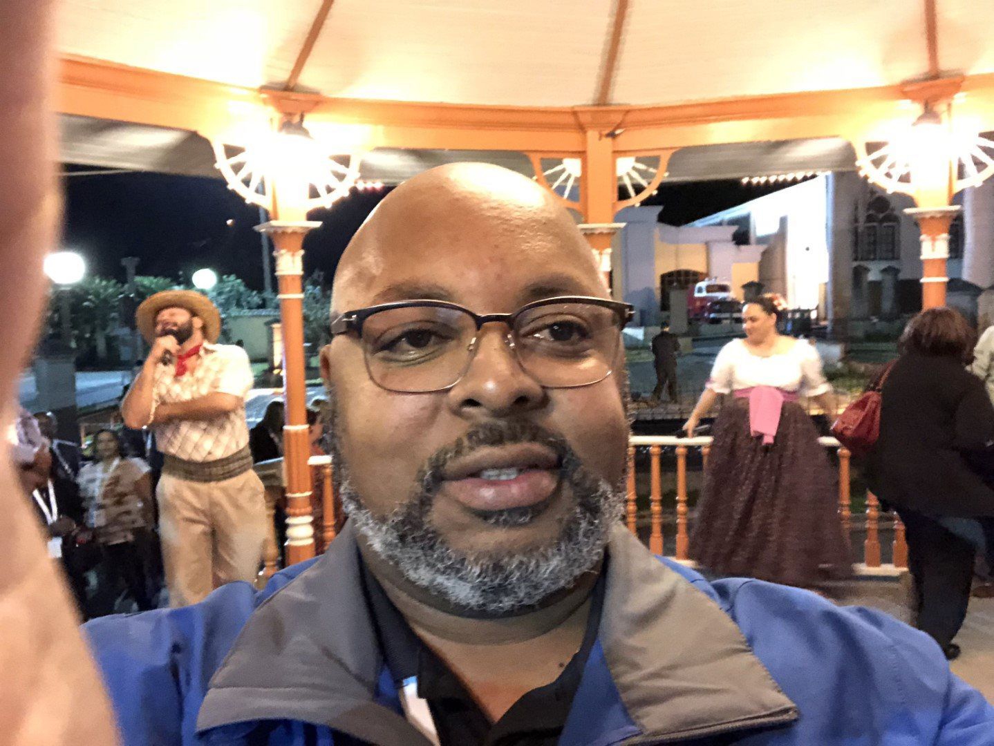 A bald man with glasses and a beard is taking a selfie