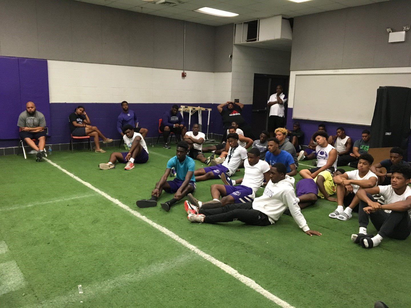 A group of people are sitting on the grass in a gym.