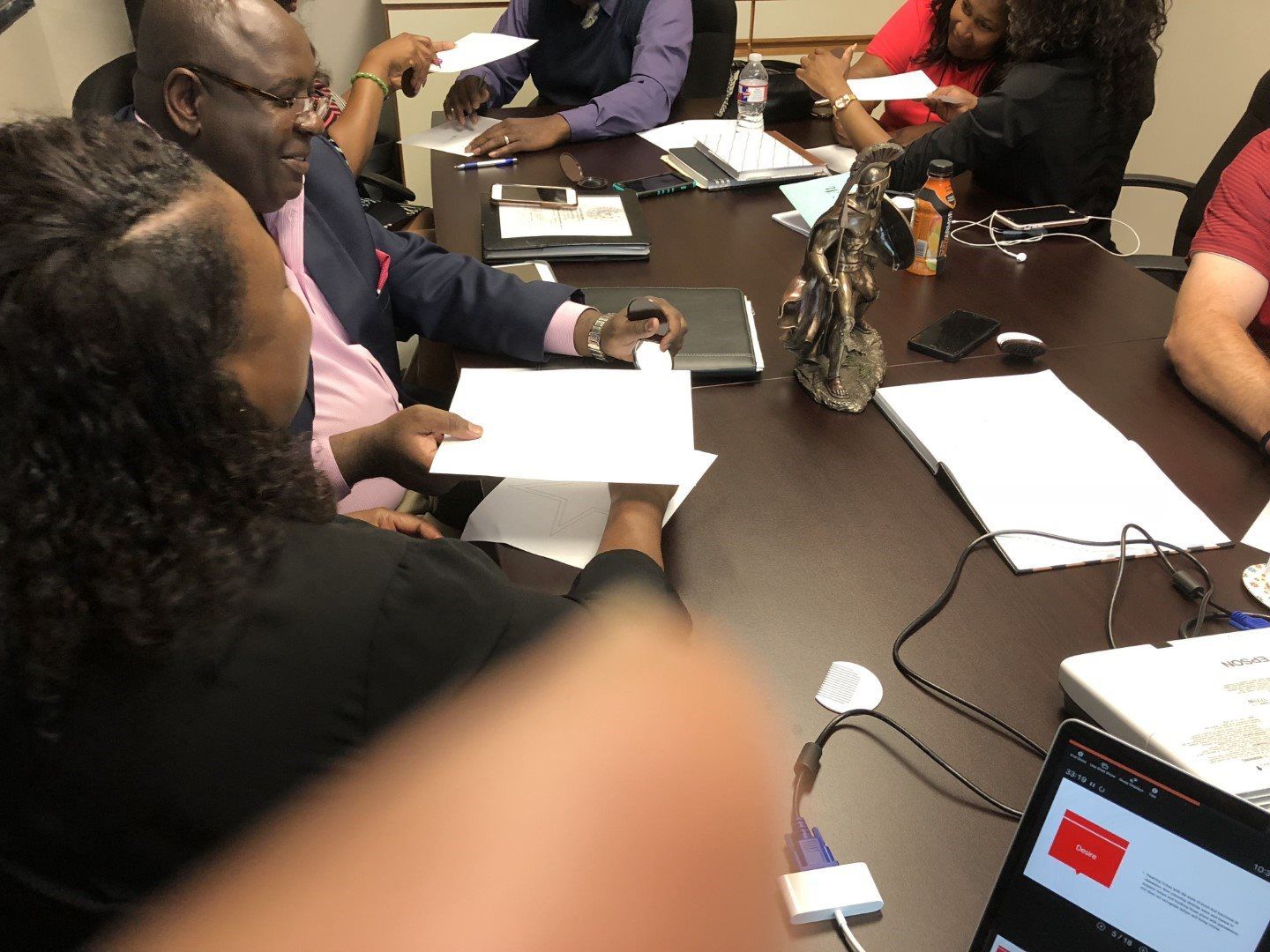 A group of people are sitting around a table with laptops and papers