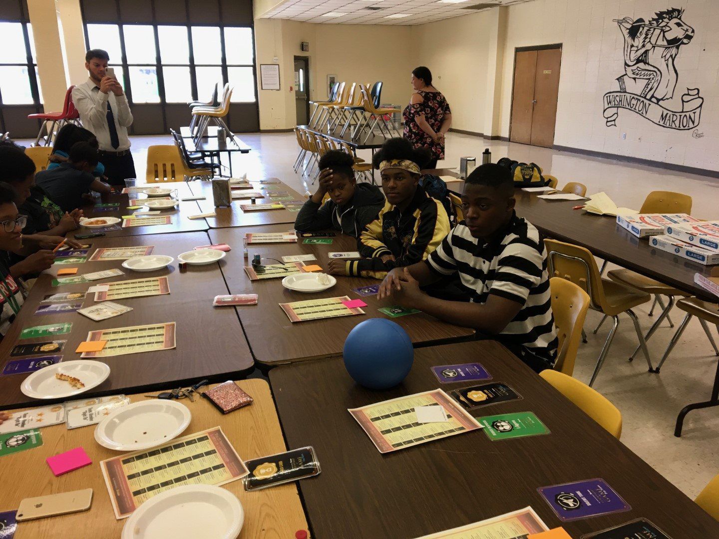 A group of people are sitting at tables with plates and cards on them.