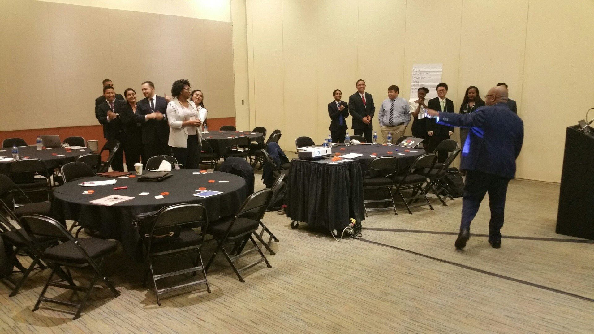 A group of people are standing around tables in a conference room.