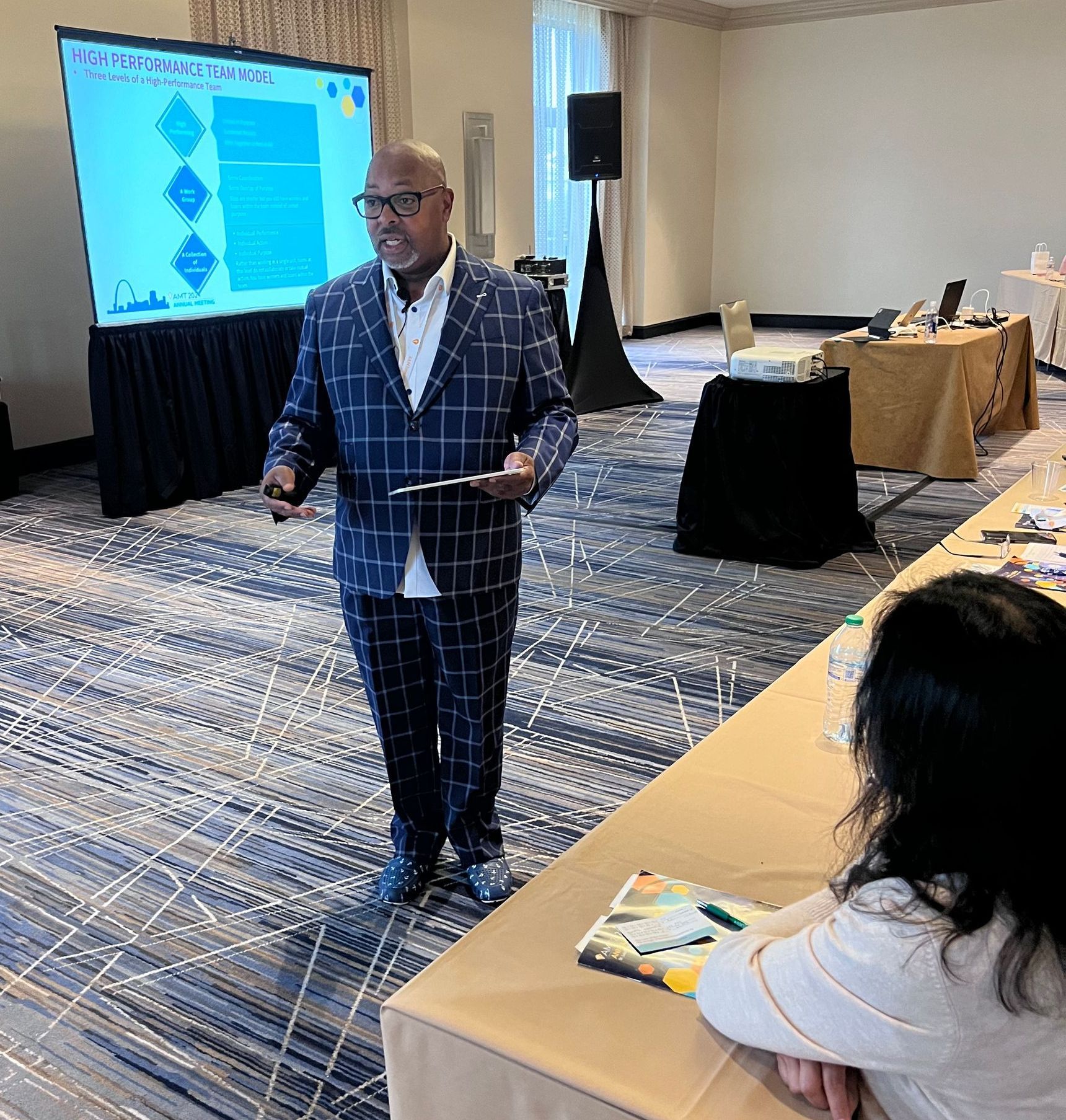 A man in a plaid suit is giving a presentation in a conference room.