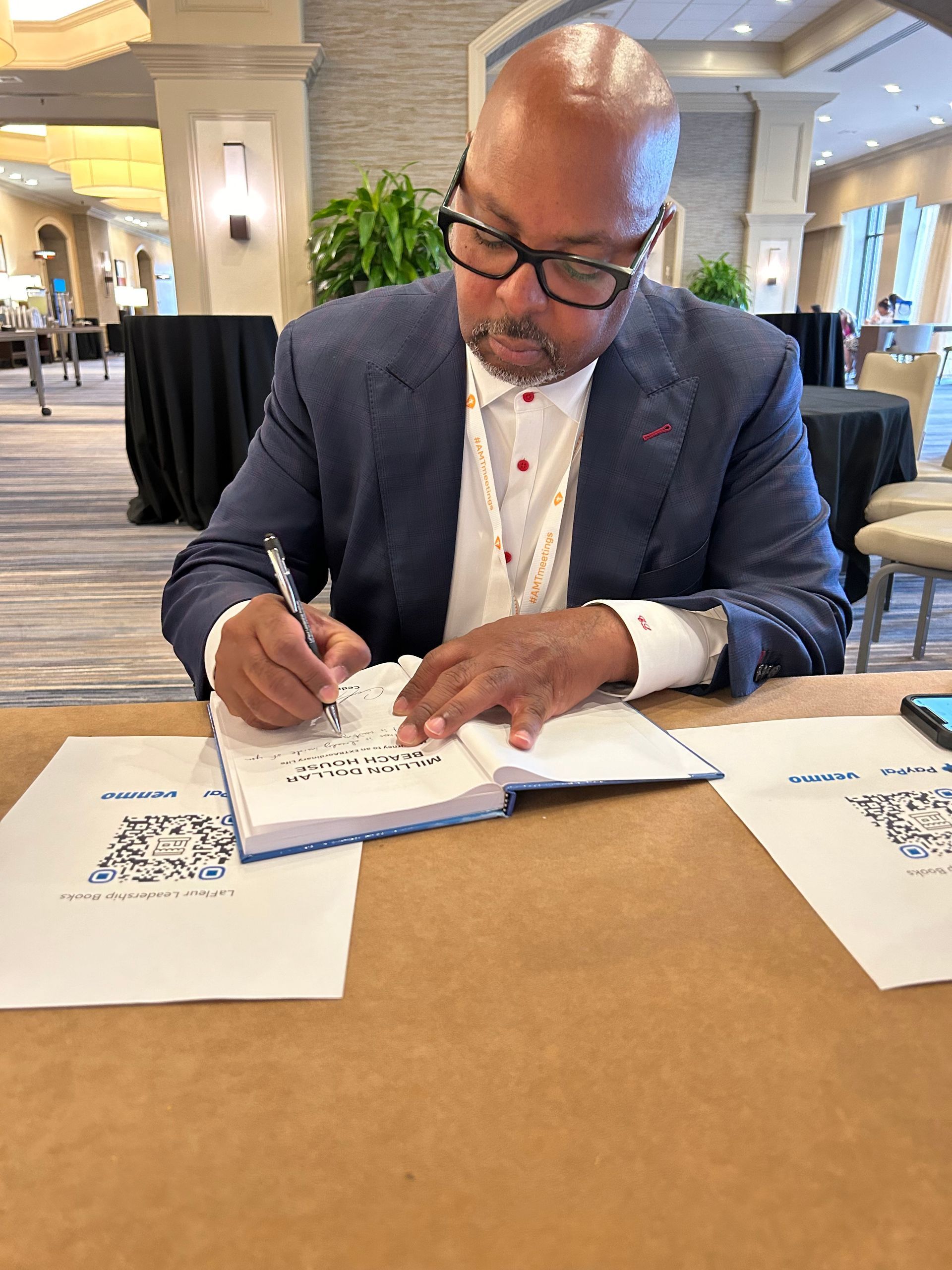 A man in a suit and bow tie is standing in front of a row of flags holding a microphone.