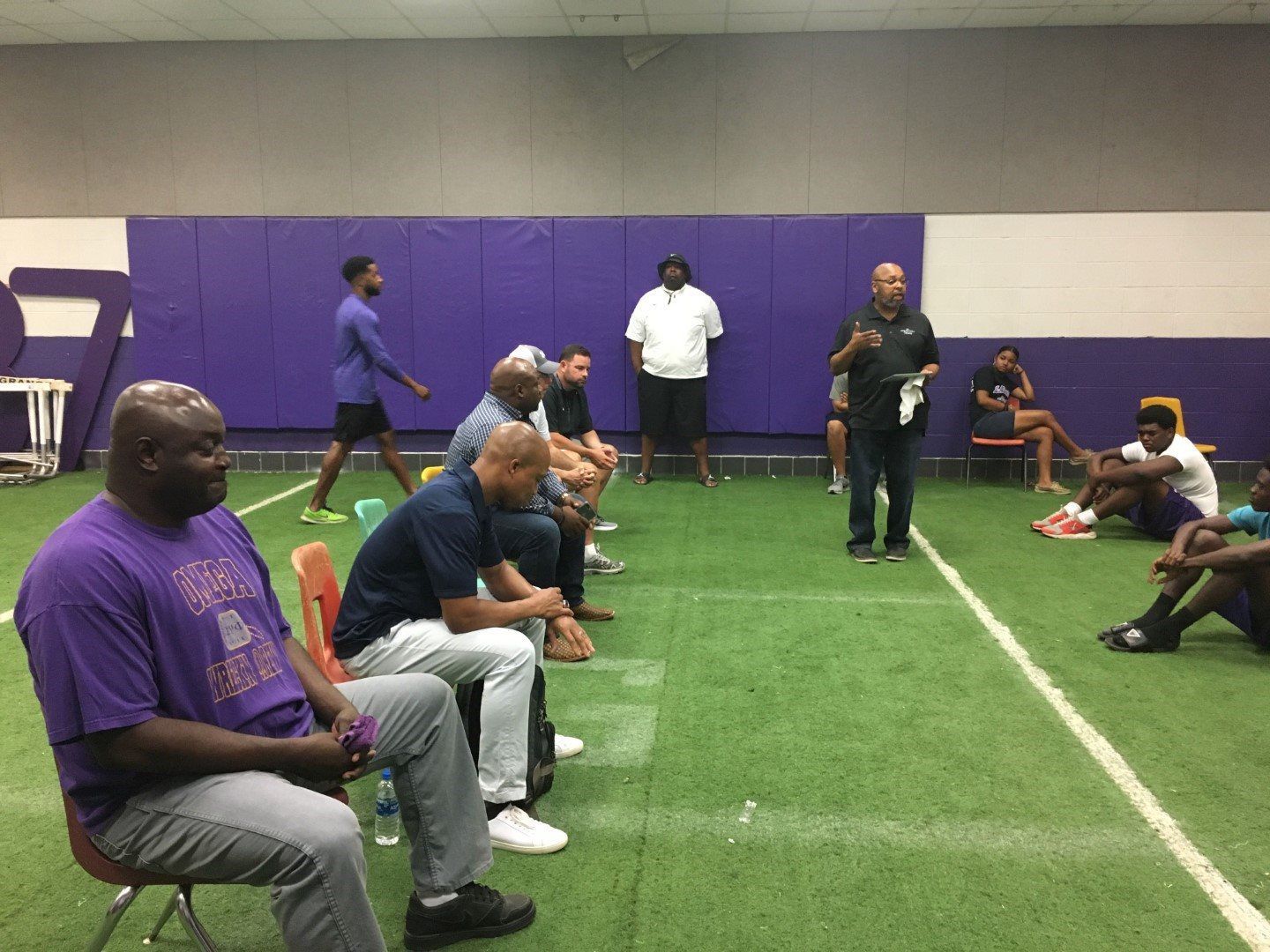 A group of men are sitting on the grass in a gym.