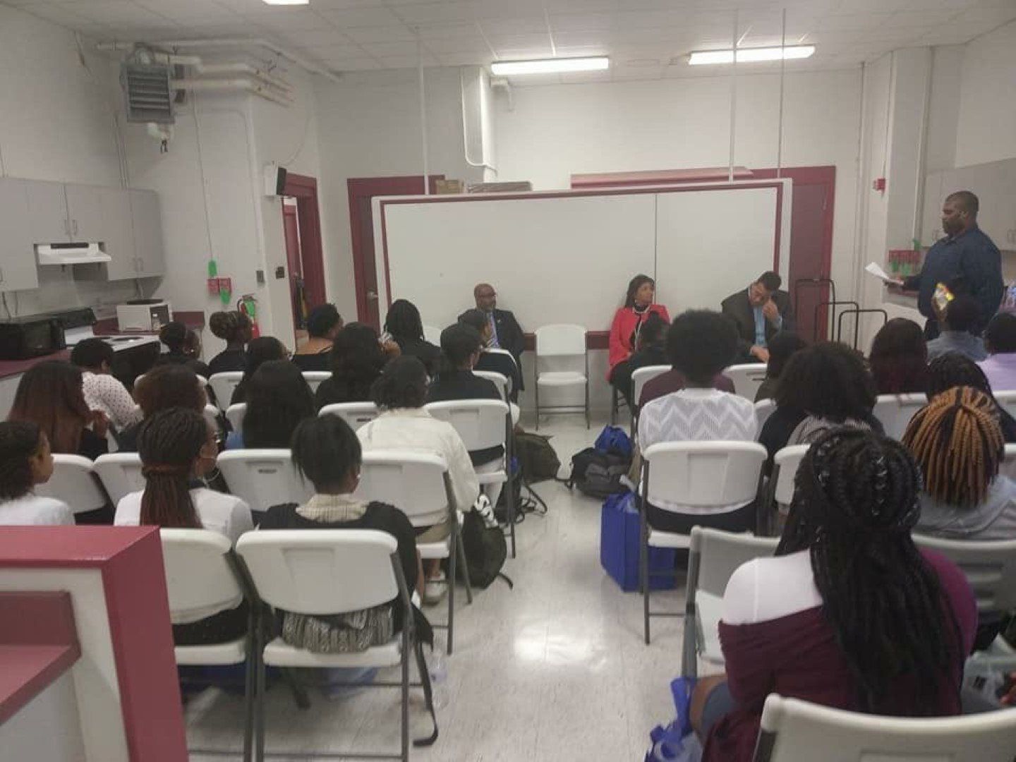 A group of people are sitting in folding chairs in a classroom.