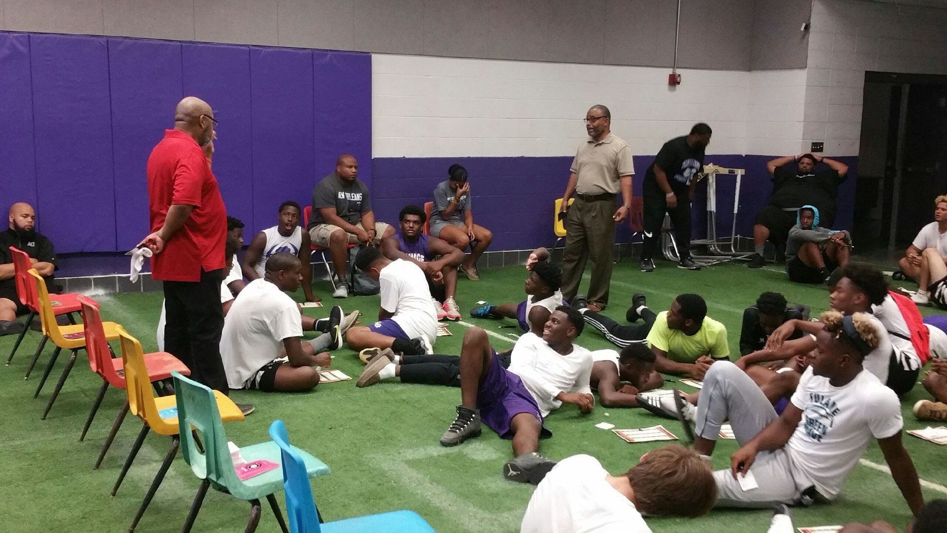 A group of people are sitting on the floor in a gym