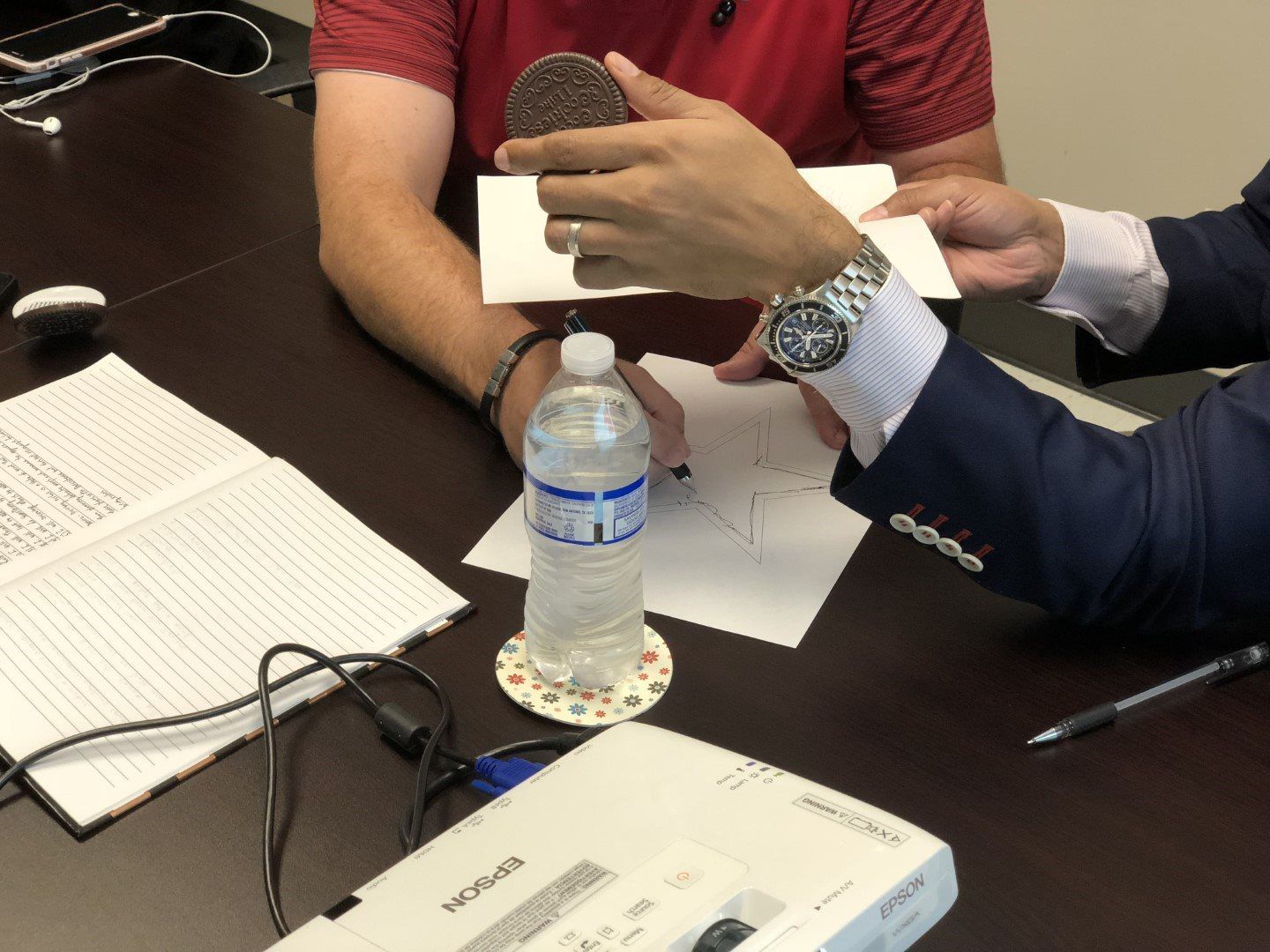 Two men are sitting at a table with a bottle of water