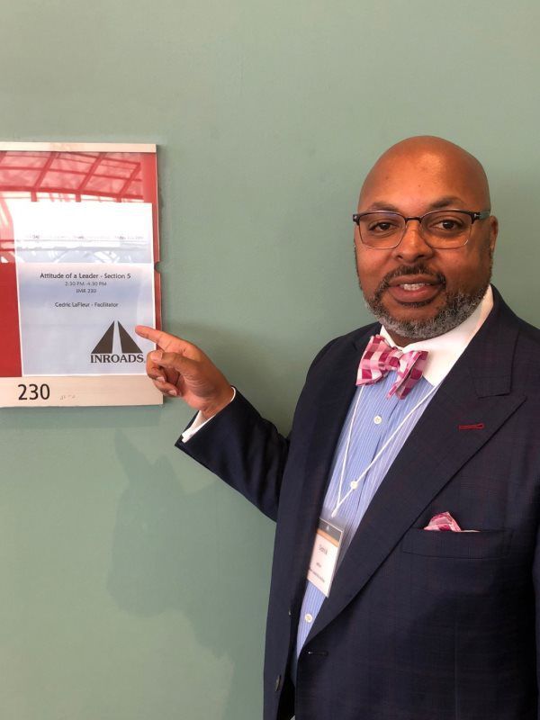 A man in a suit and bow tie is pointing at a sign that says 230