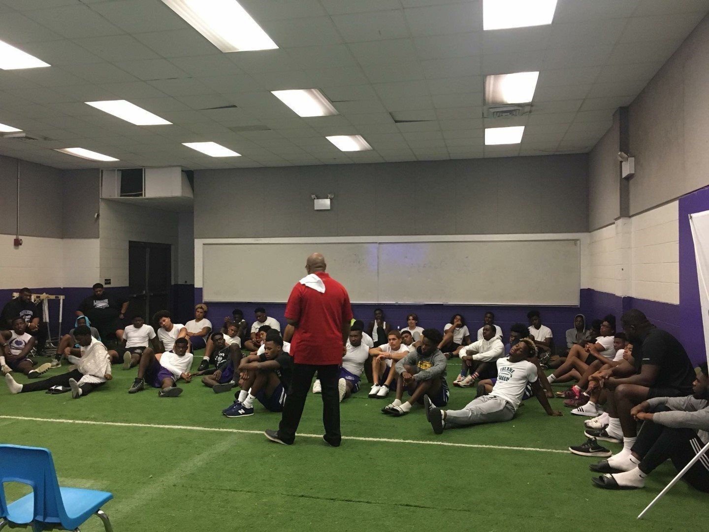 A man is standing in front of a group of people sitting on the floor.