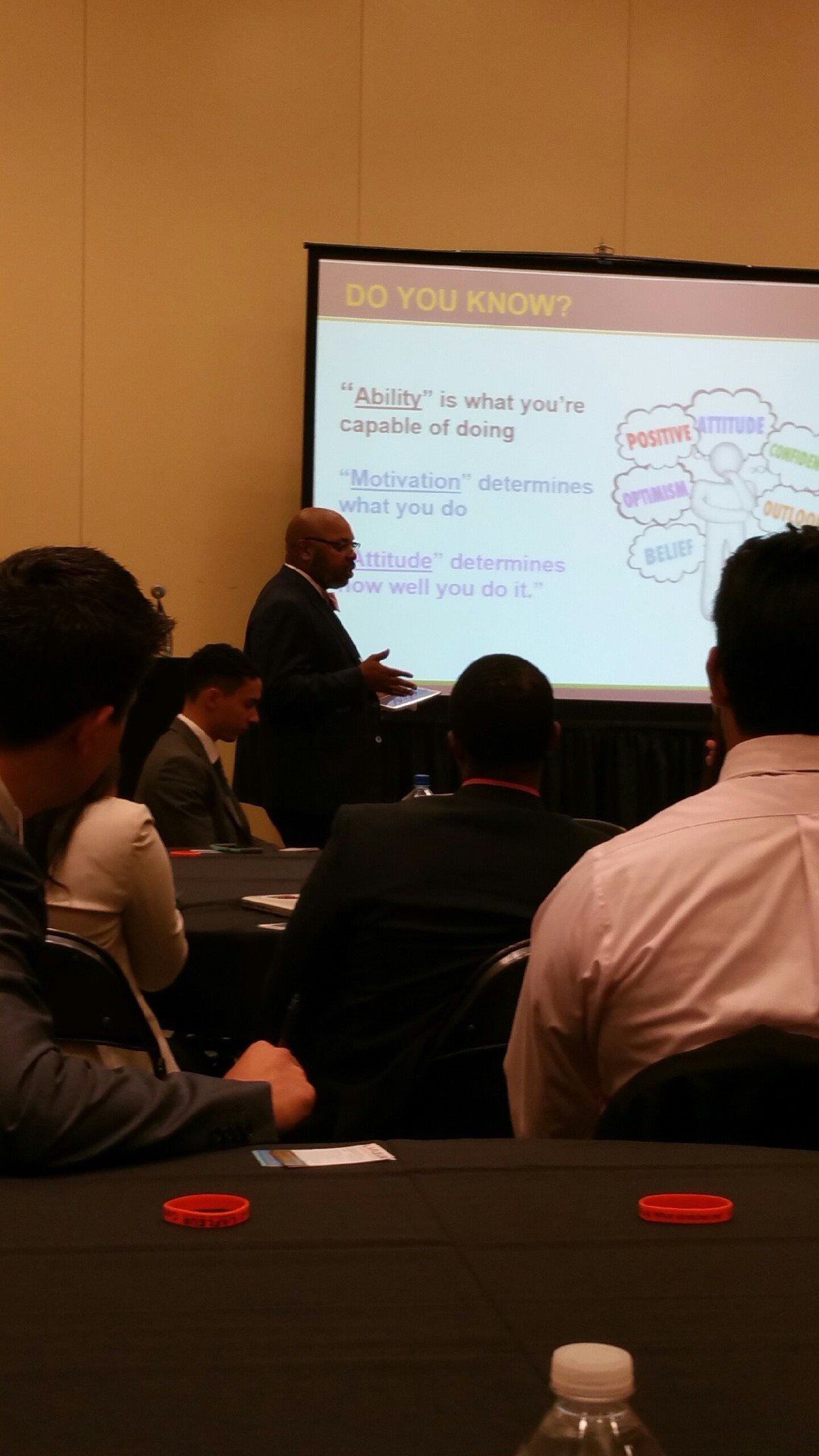A man is giving a presentation to a group of people in front of a screen that says do you know