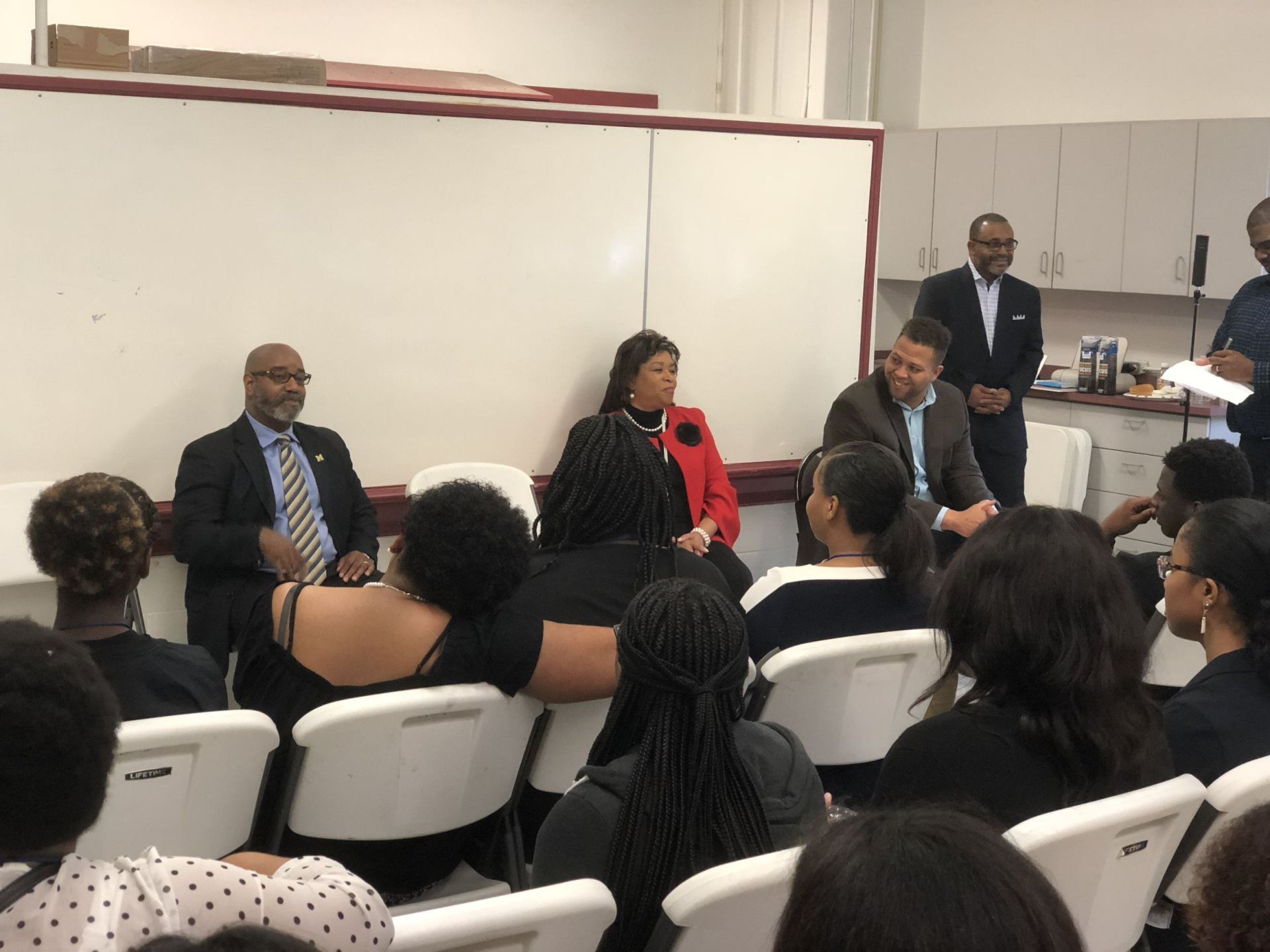 A group of people are sitting in chairs in front of a white board.