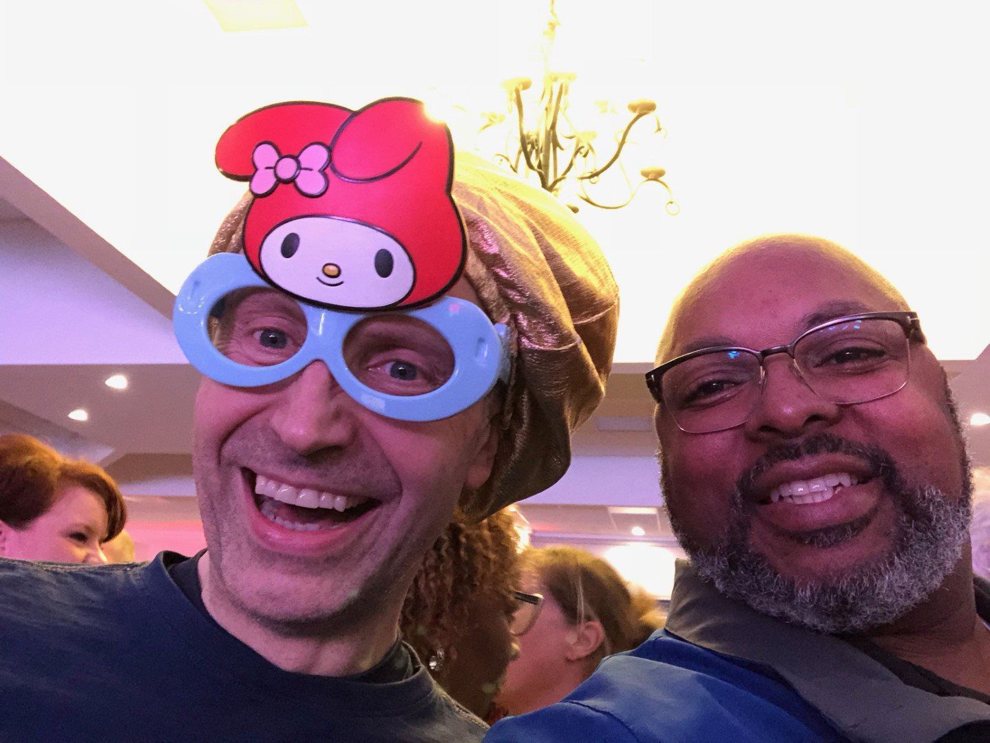 Two men are posing for a picture with one wearing a hello kitty mask