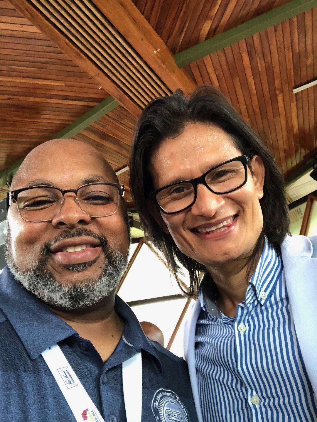 Two men are posing for a picture together in a room with a wooden ceiling.