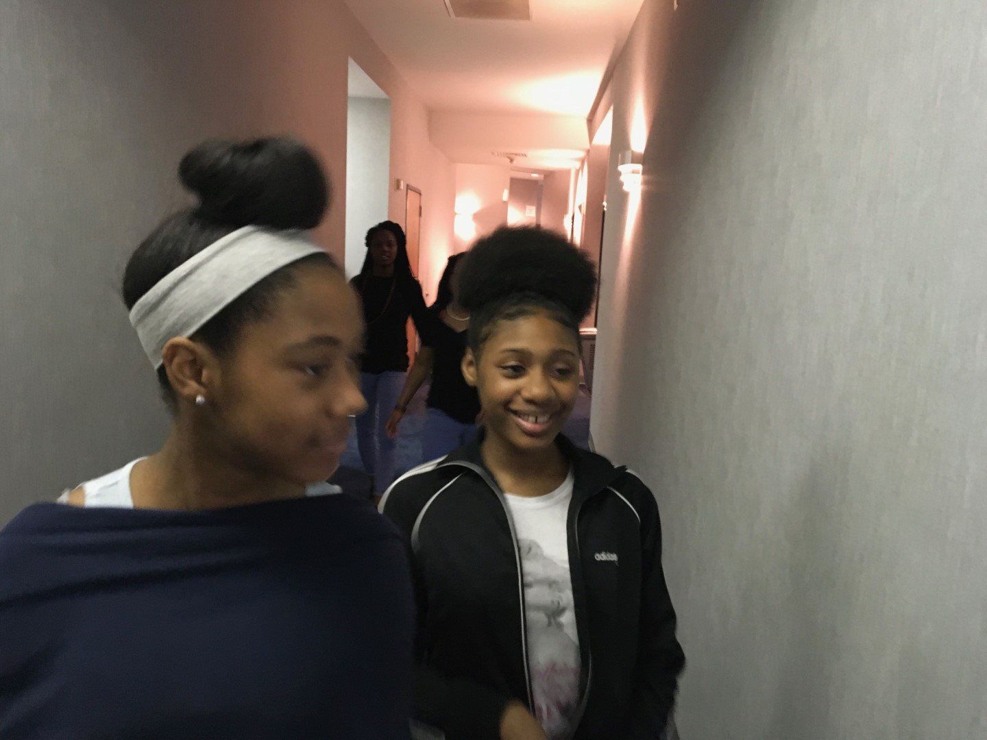 Two girls are standing next to each other in a hallway.