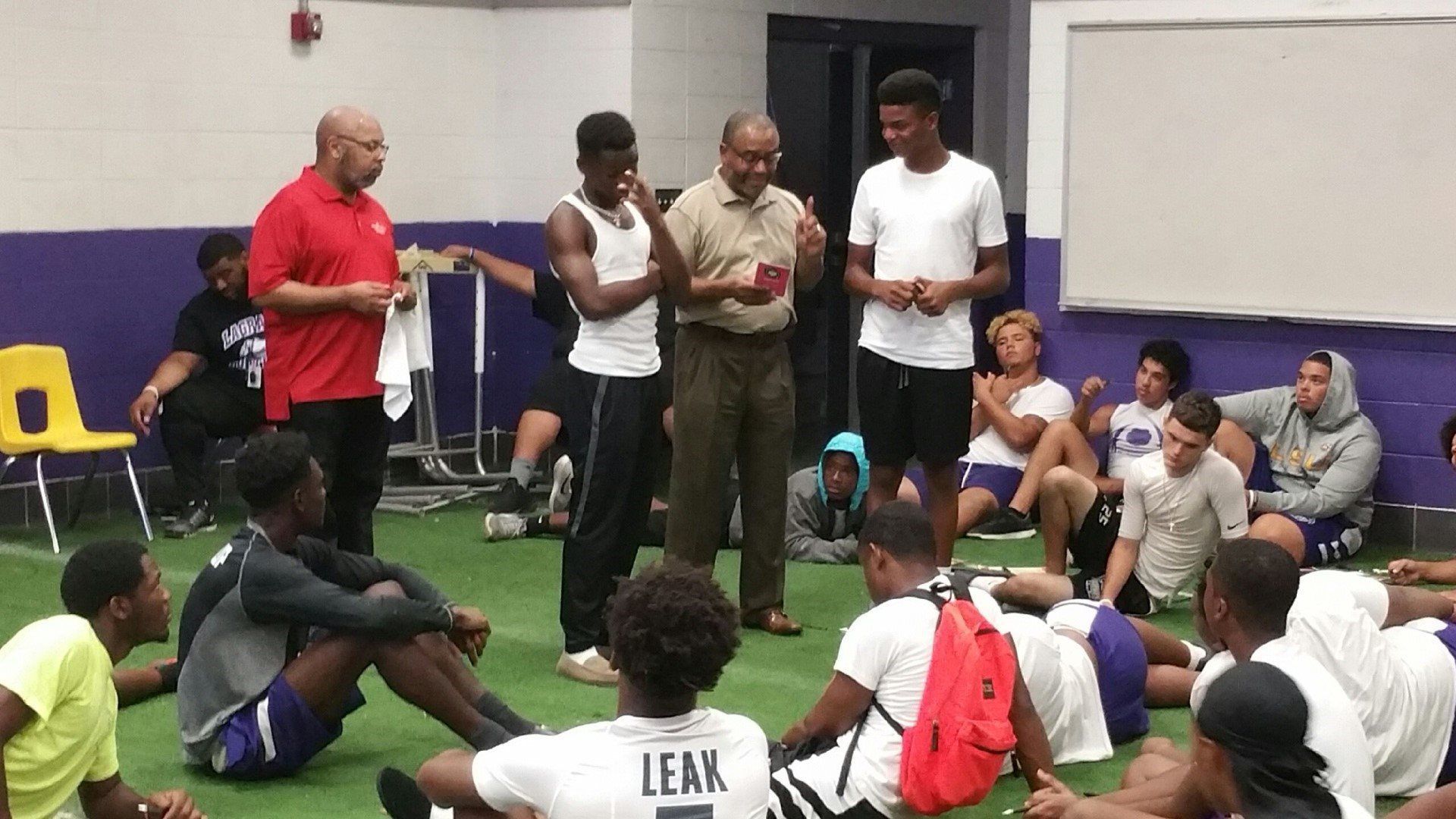 A group of young men are sitting in a circle and one of them is wearing a shirt that says leak