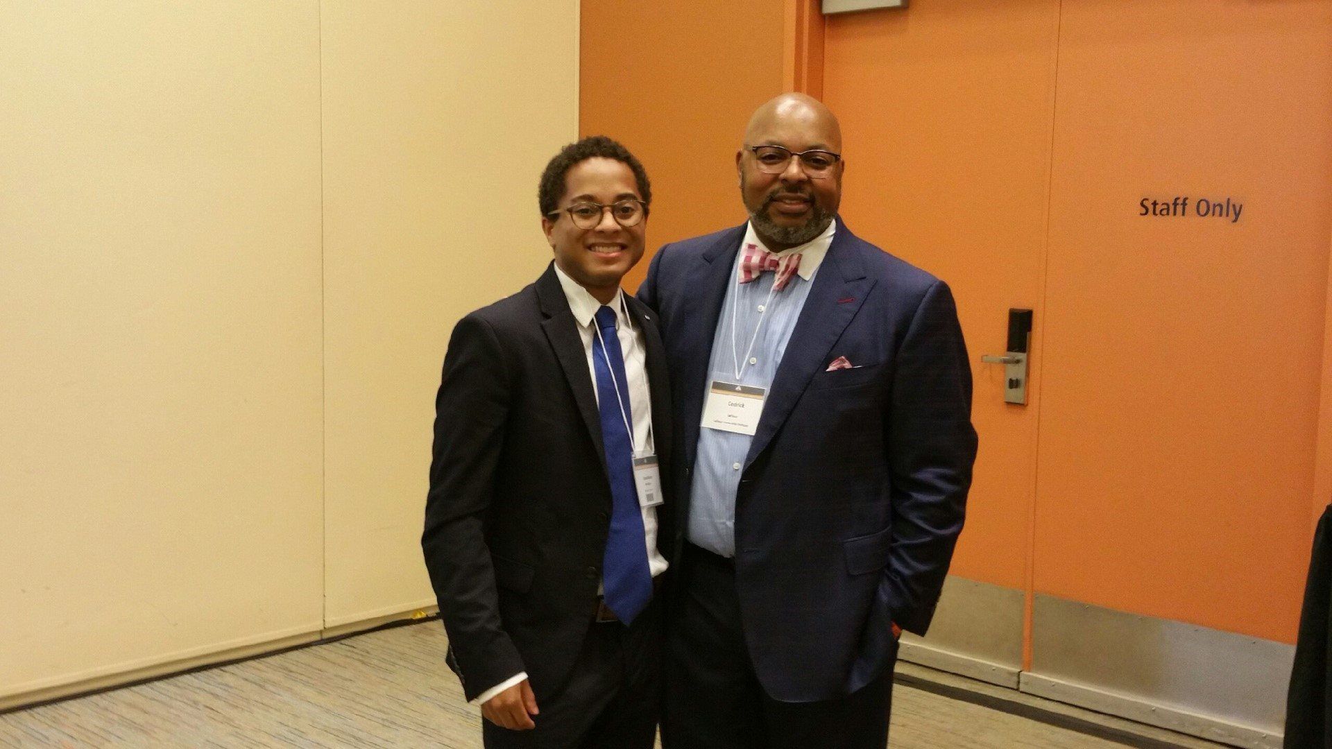 Two men in suits and bow ties are posing for a picture in front of an orange door.