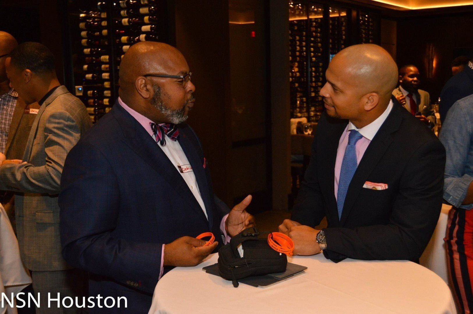 Two men in suits are sitting at a table talking to each other.