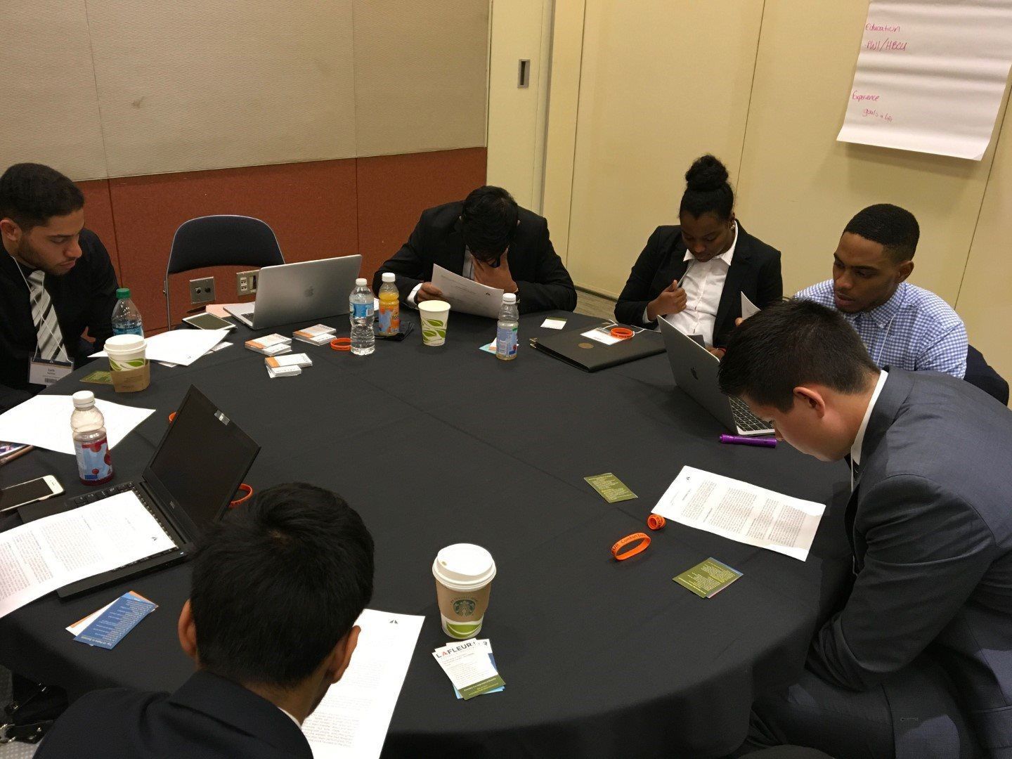 A group of people are sitting around a table with laptops.