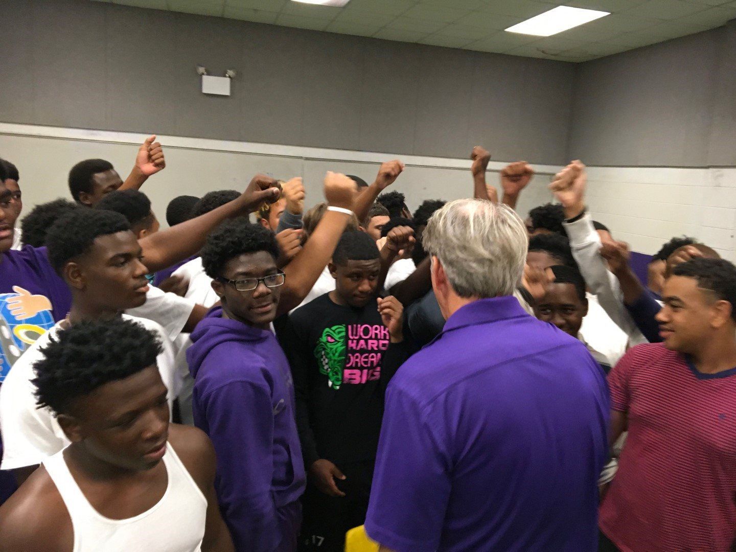 A man in a purple shirt is talking to a group of young men