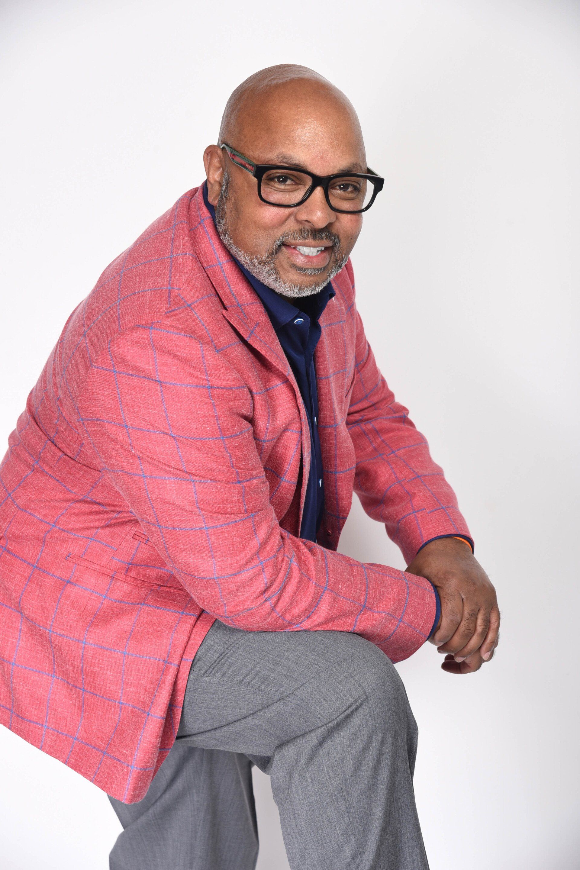 A man wearing glasses and a pink jacket is kneeling down.
