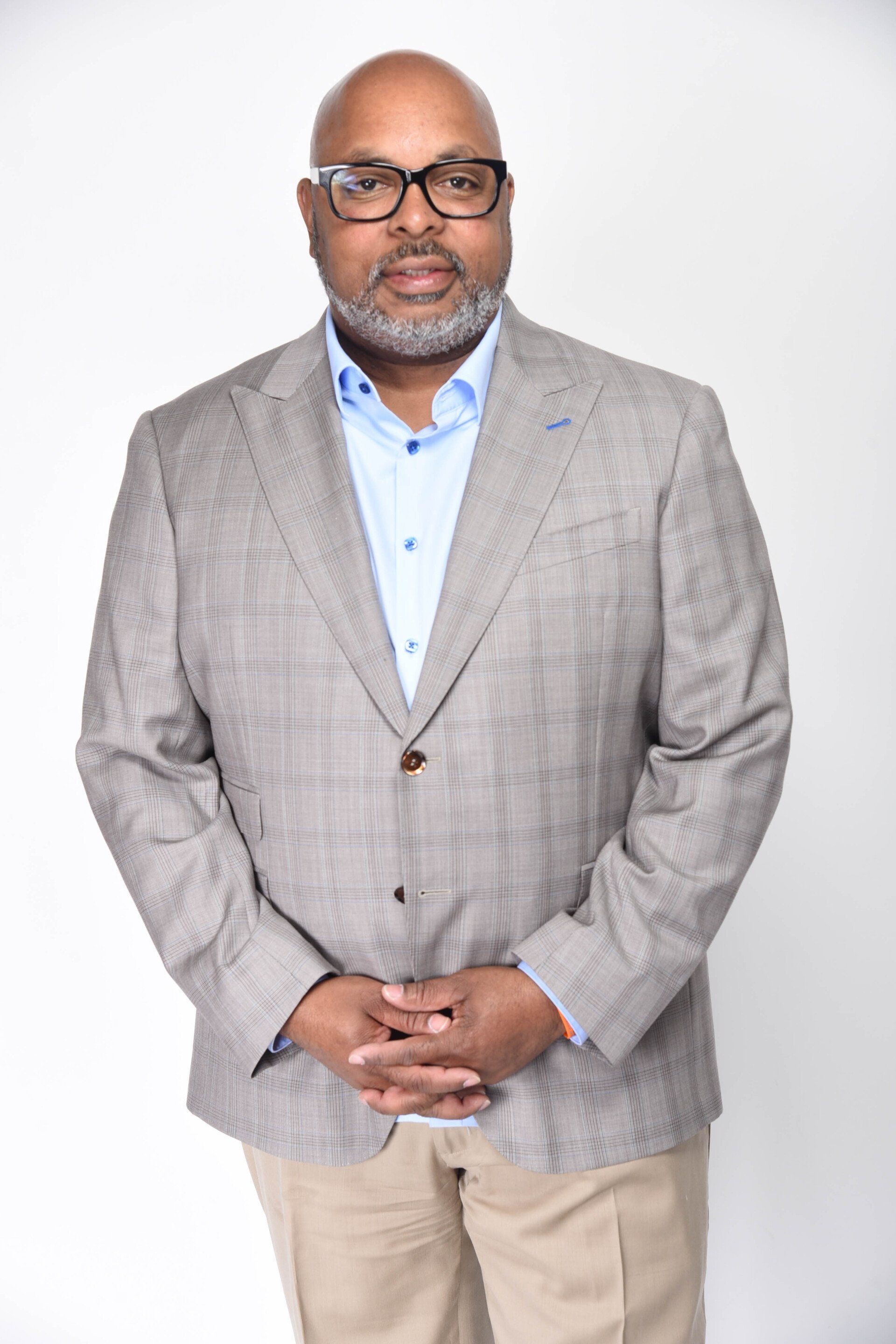 A man in a suit and glasses is standing with his hands folded.